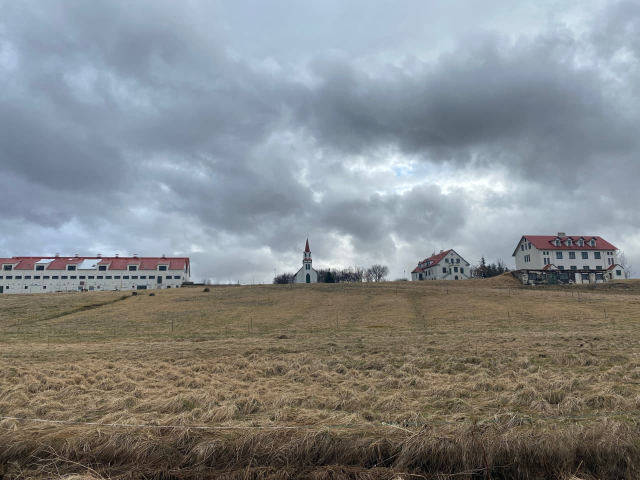 Hvanneyri church and old school buildings above fields under heavy clouds.