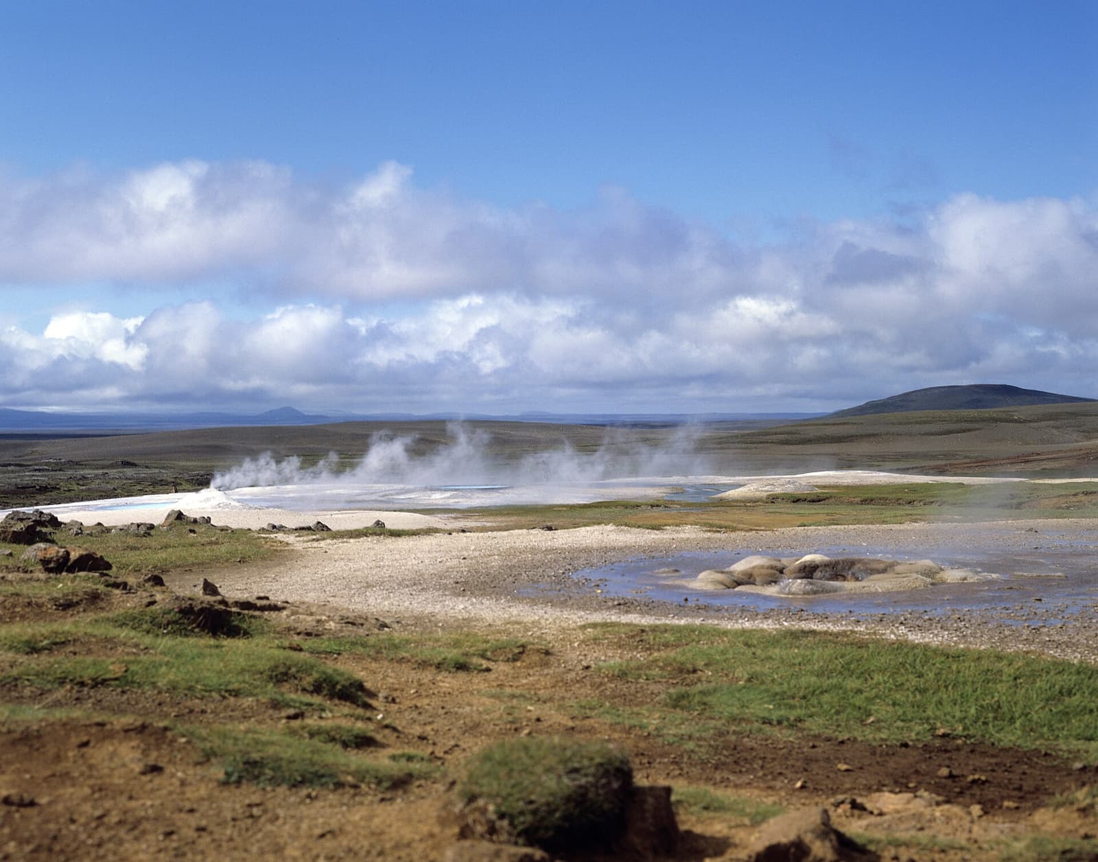 Steam drifting across the Hveravellir geothermal field with low highland hills behind it.