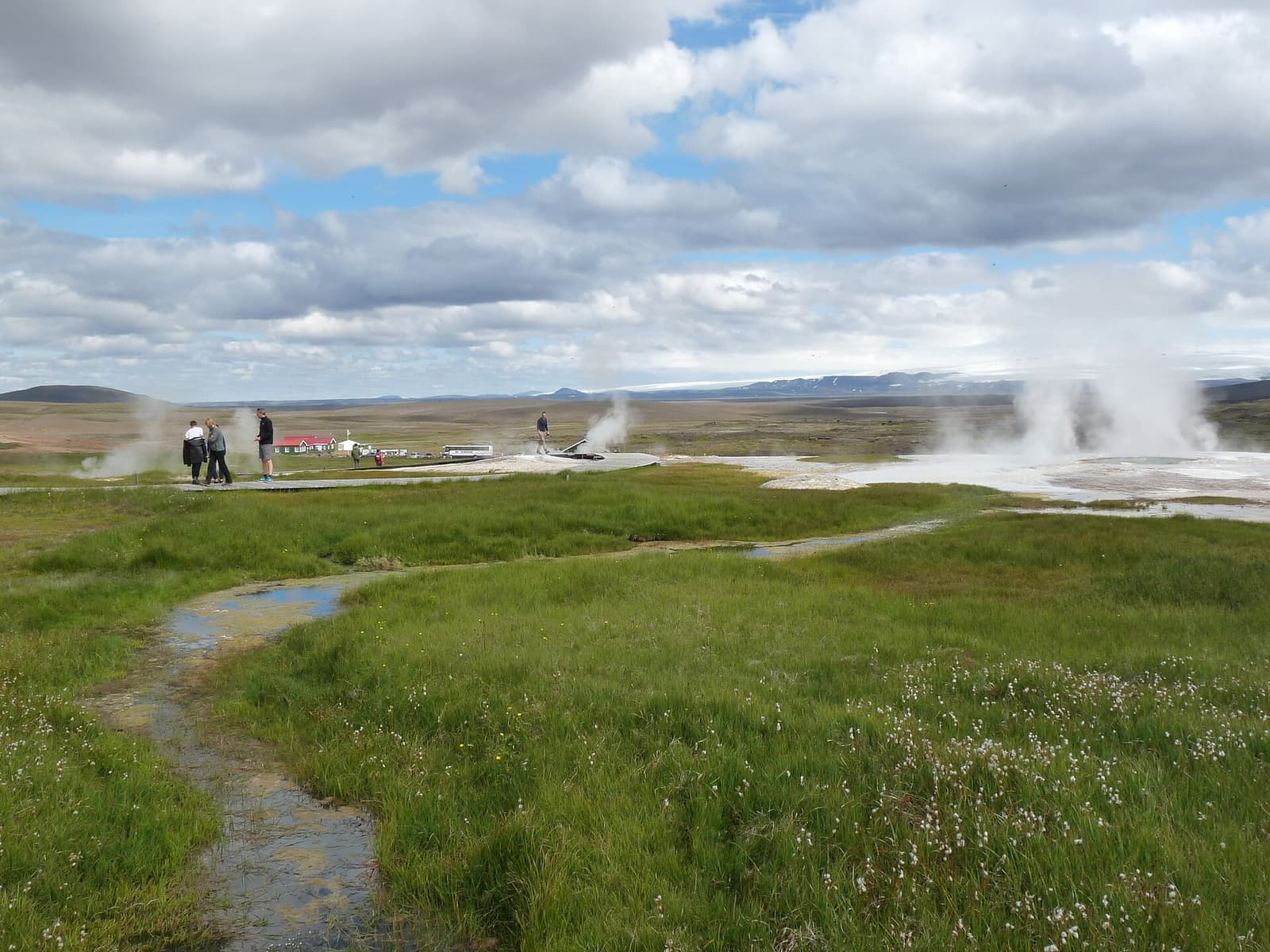 Steam rising from the Hveravellir geothermal field with wooden paths and highland mountains in the distance.