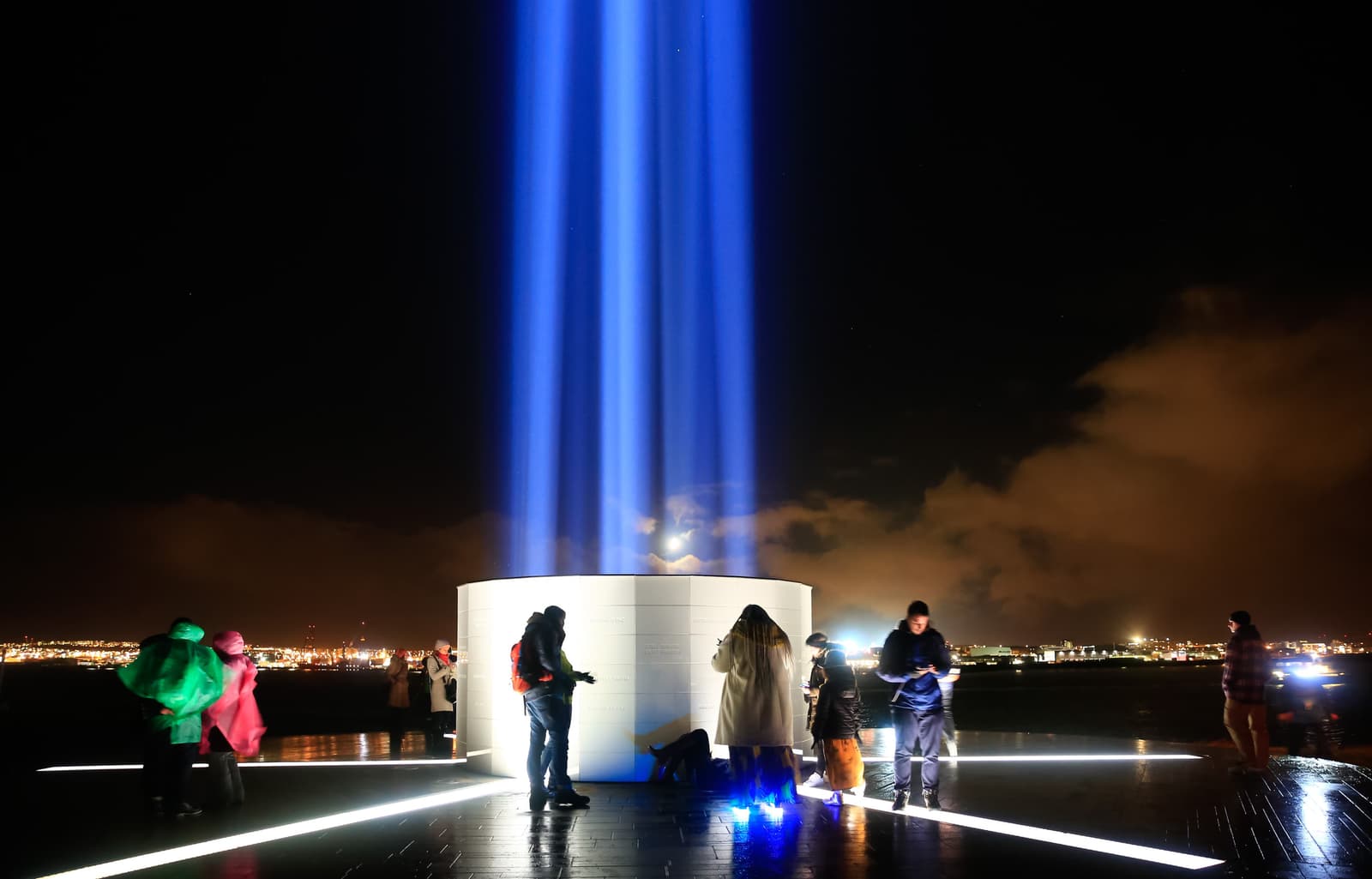 Visitors standing around the lit Imagine Peace Tower on Viðey at night