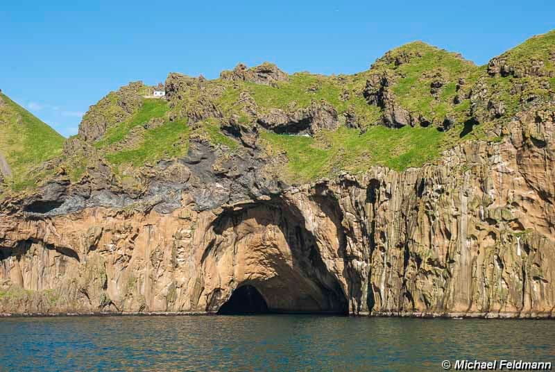 Klettshellir cave opening at the base of Ystiklettur cliffs above blue water on Heimaey.