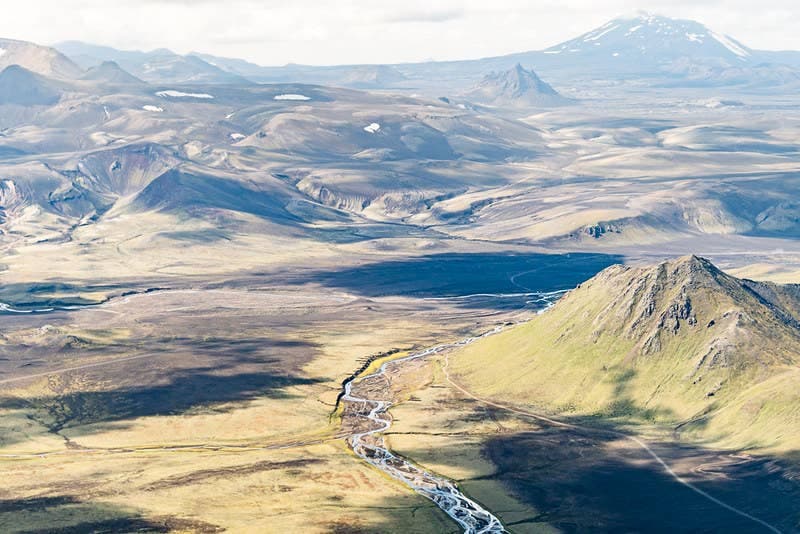 Wide Highland view of Krakatindur below Hekla with lava fields, pale hills, and a braided stream.