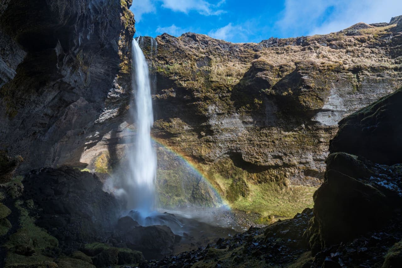 Kvernufoss waterfall dropping into Kvernugil canyon with a rainbow in the spray.