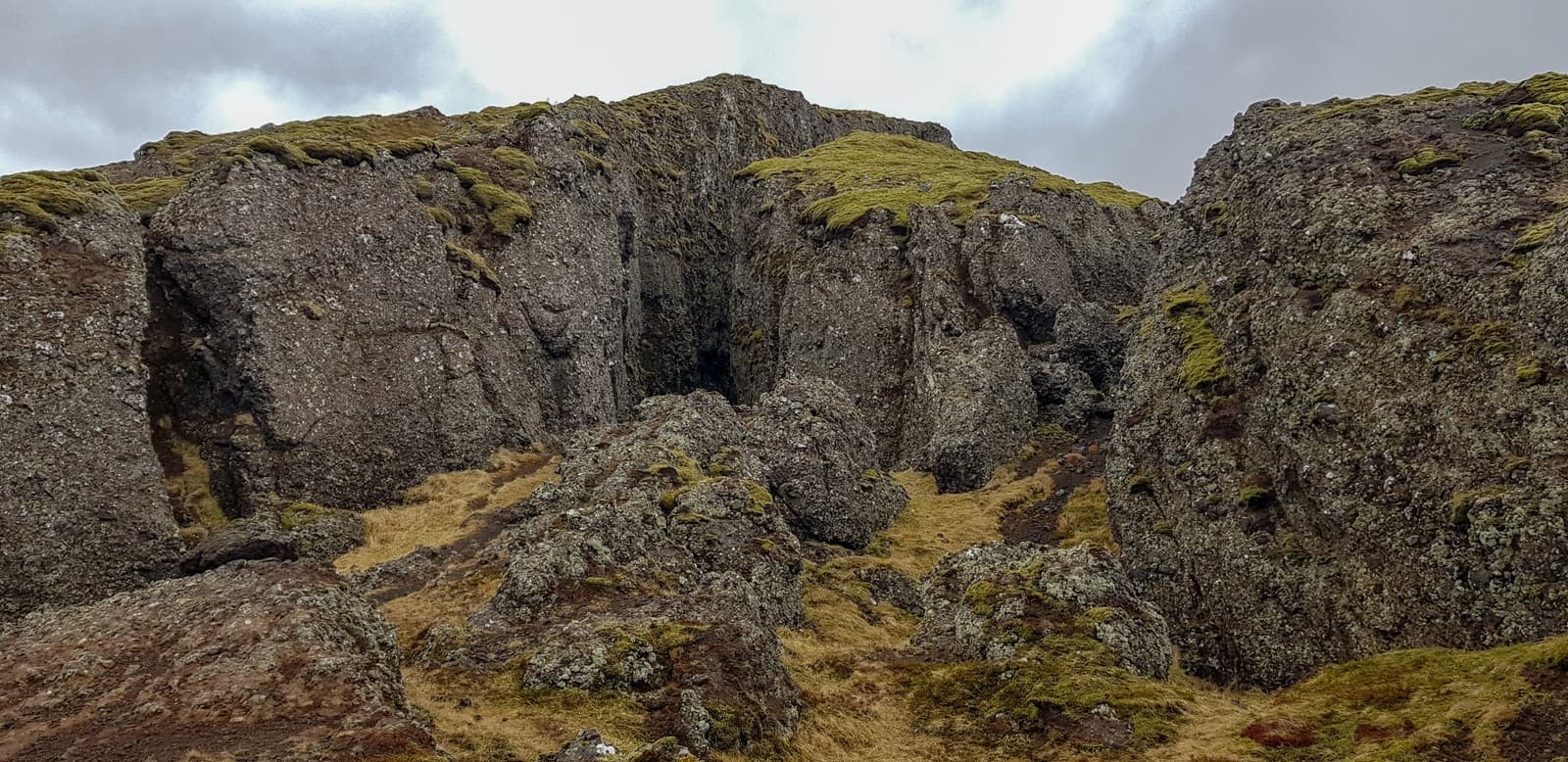 Exterior view of Lambafellsgjá showing the fissure opening in mossy volcanic rock.