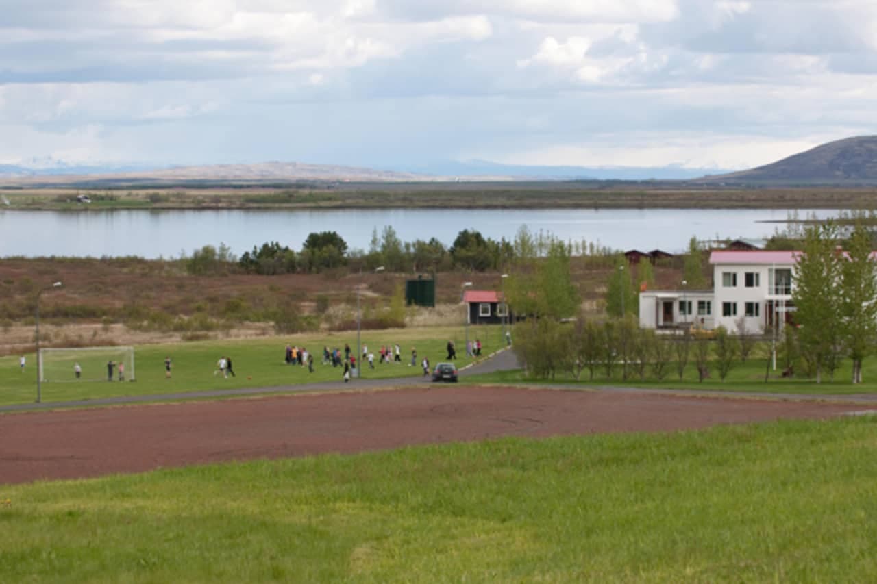 Laugarvatn village buildings and a sports field beside Lake Laugarvatn under cloudy South Iceland skies.