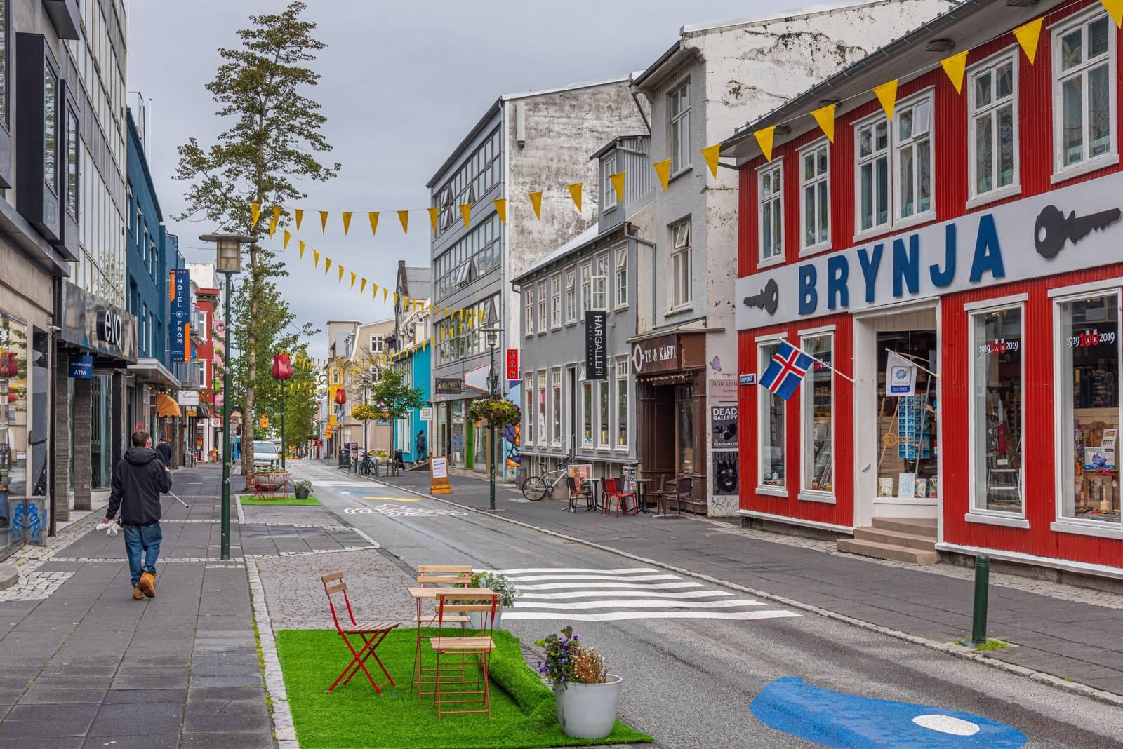 Laugavegur street in Reykjavík with colorful storefronts, flags, and a pedestrian crossing.