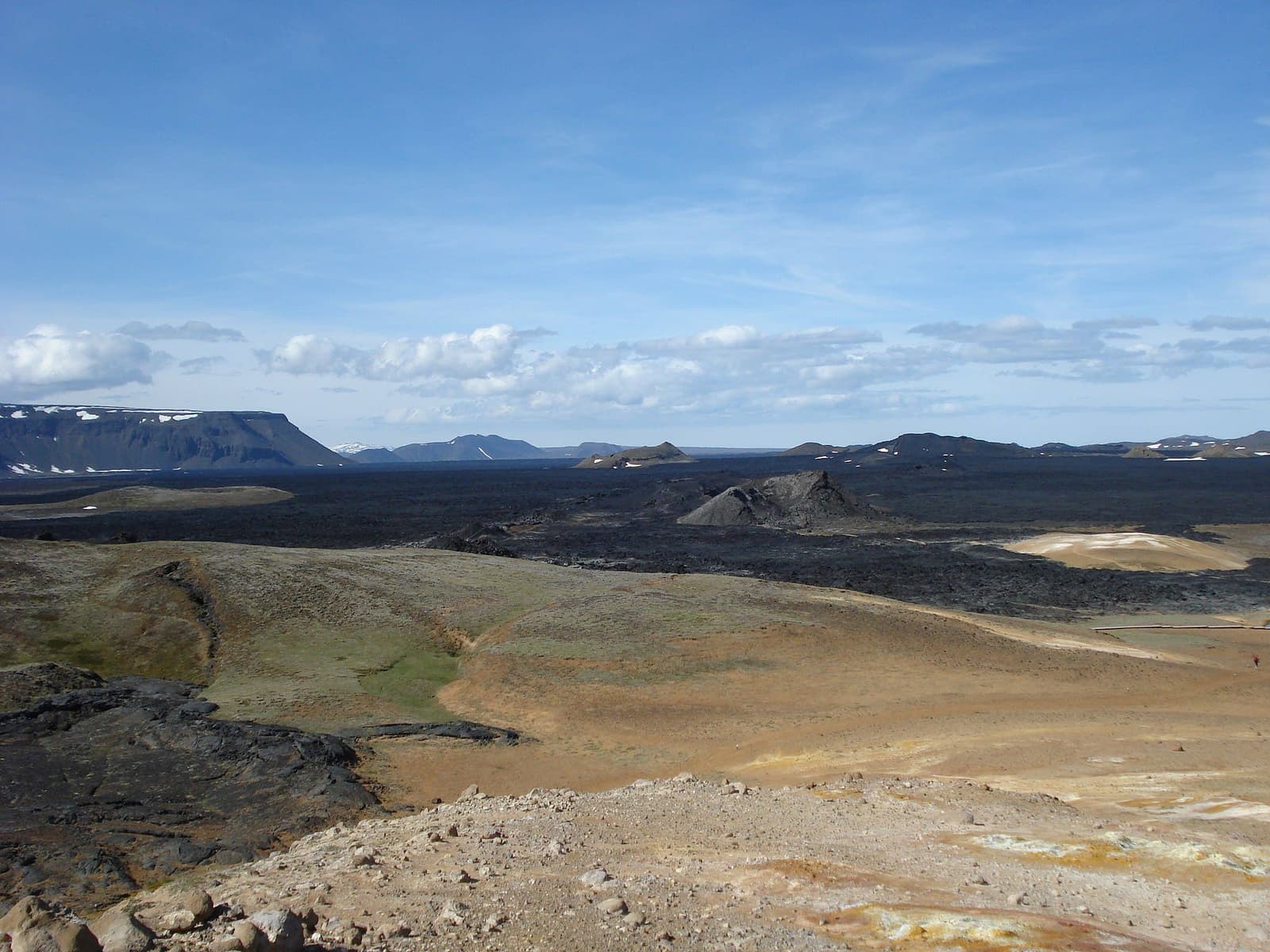 Wide view across the black lava field, crater slopes, and pale geothermal ground at Leirhnjúkur near Krafla.