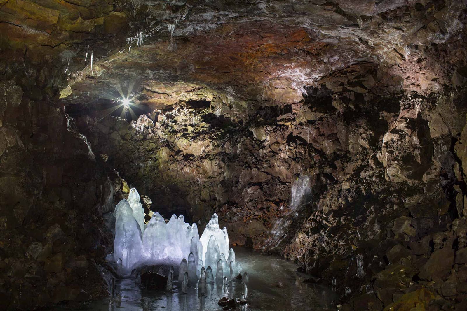 Lofthellir cave chamber with clear ice formations below a rough brown lava ceiling.