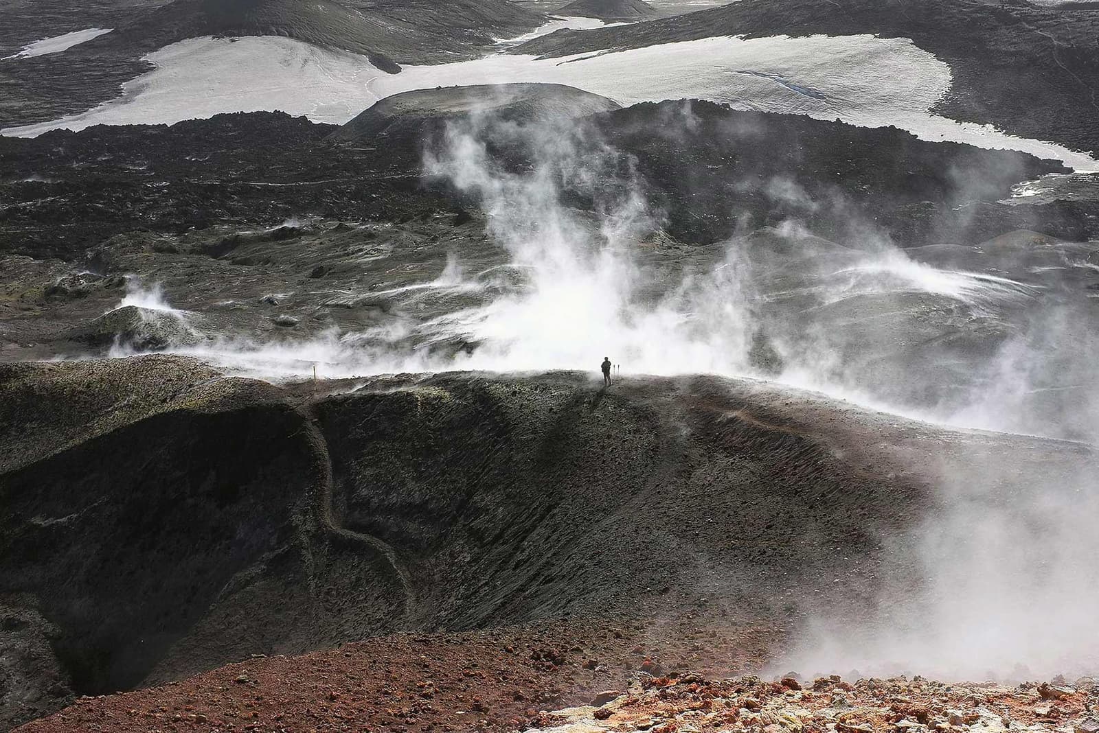 A hiker on the exposed volcanic pass of Fimmvörðuháls near snowy glacier edges.