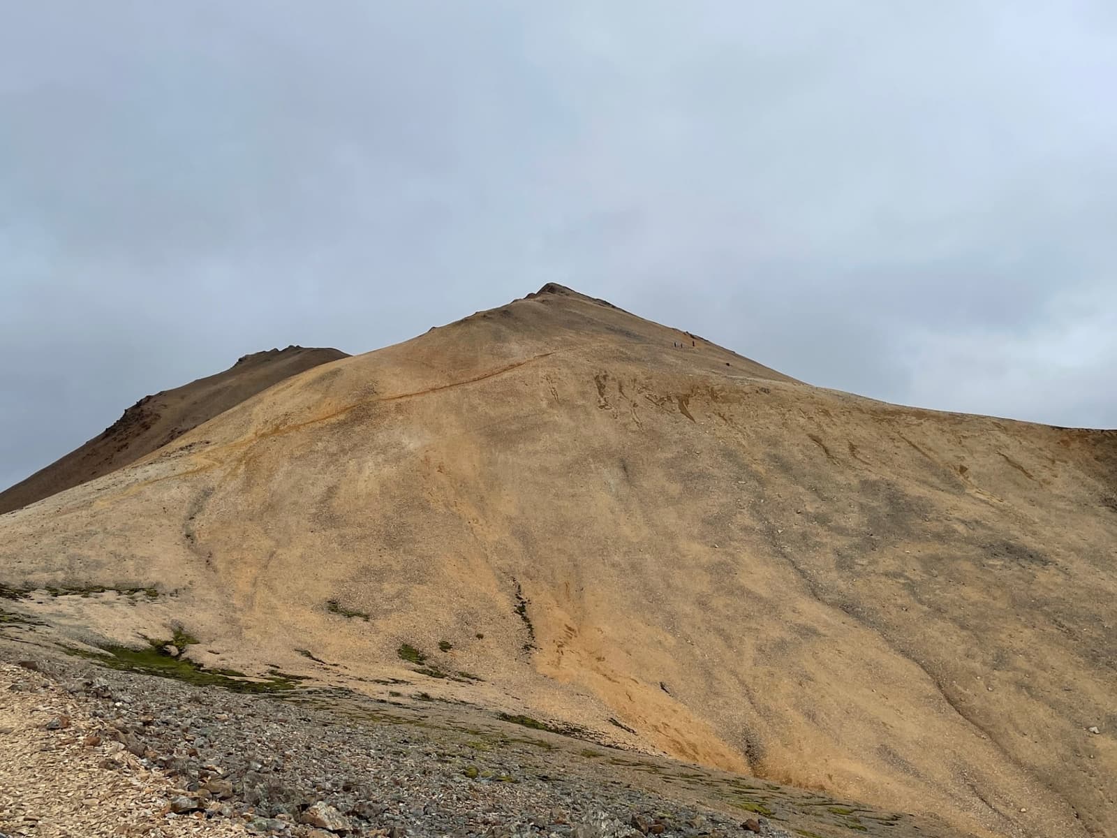 A pale golden rhyolite slope on Móskarðshnjúkar with tiny hikers near the ridge.