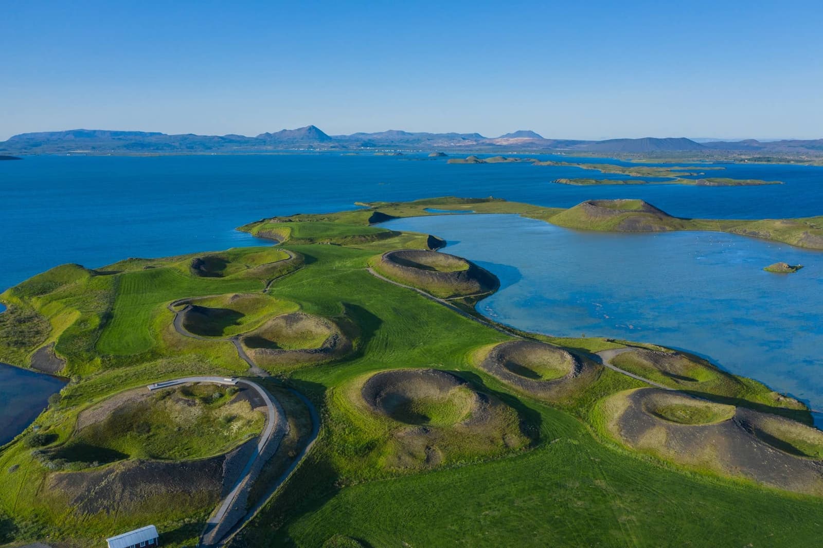 Bright view across Lake Mývatn with low green pseudocraters and volcanic hills.