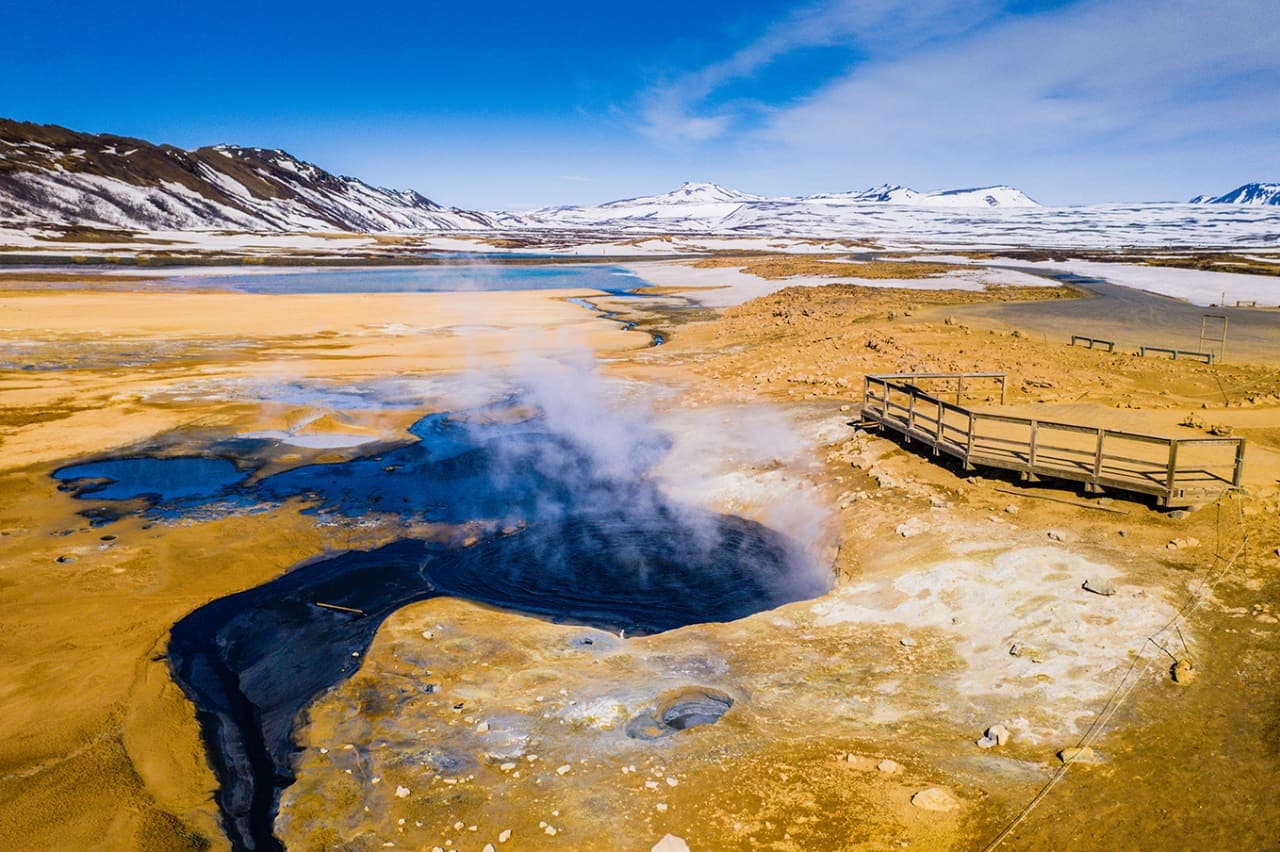 Steaming geothermal pool, marked boardwalk, and snowy hills at Námafjall by Námaskarð.