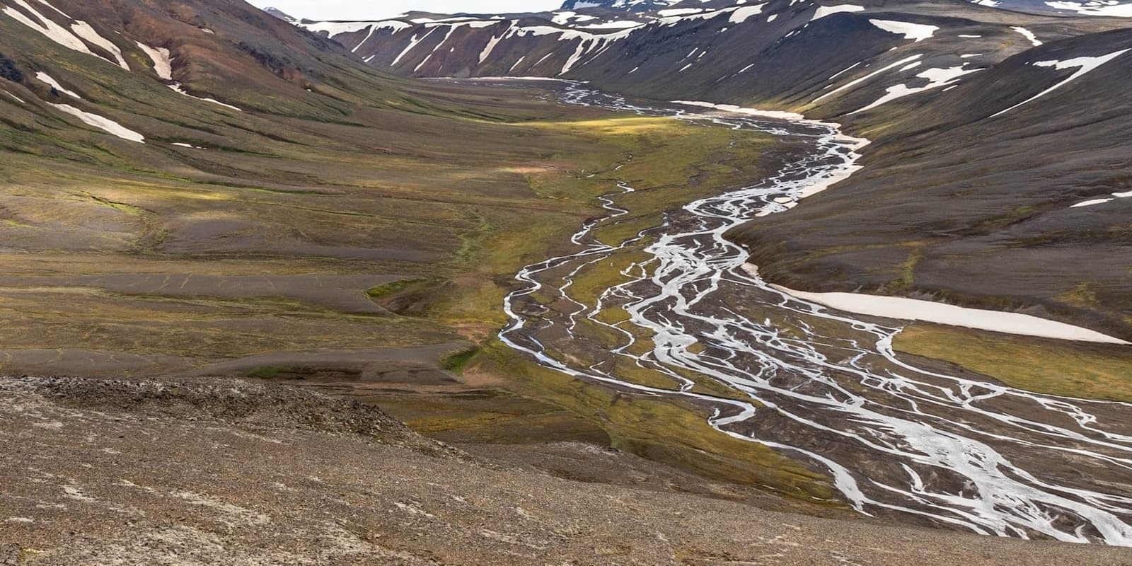 Nýjadalsá river braiding through the remote Nýidalur valley between dark snow-streaked Highlands slopes.