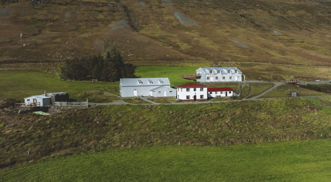 Aerial view of The Wilderness Center buildings in Fljótsdalur with green fields and brown highland-edge slopes around the site.