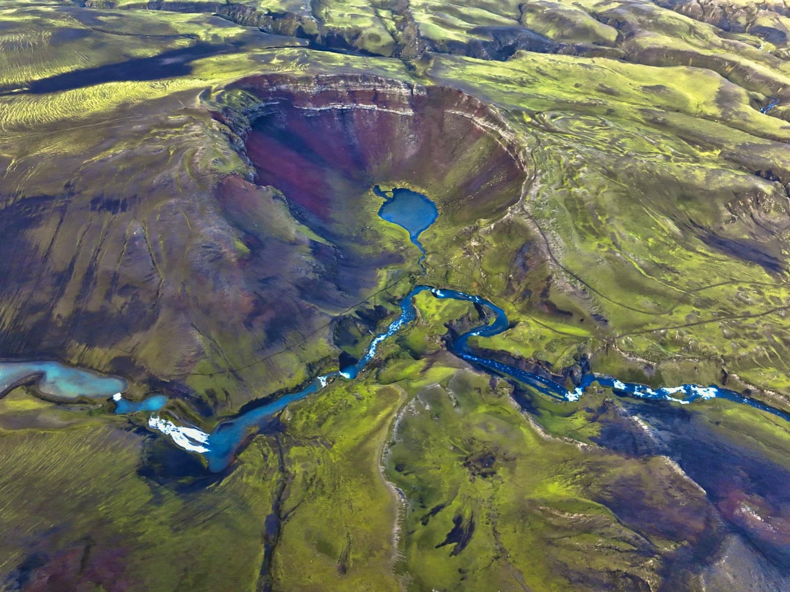 Aerial view of Rauðibotn Crater with red slopes, green moss, a small lake, and Hólmsá channels in the Highlands.