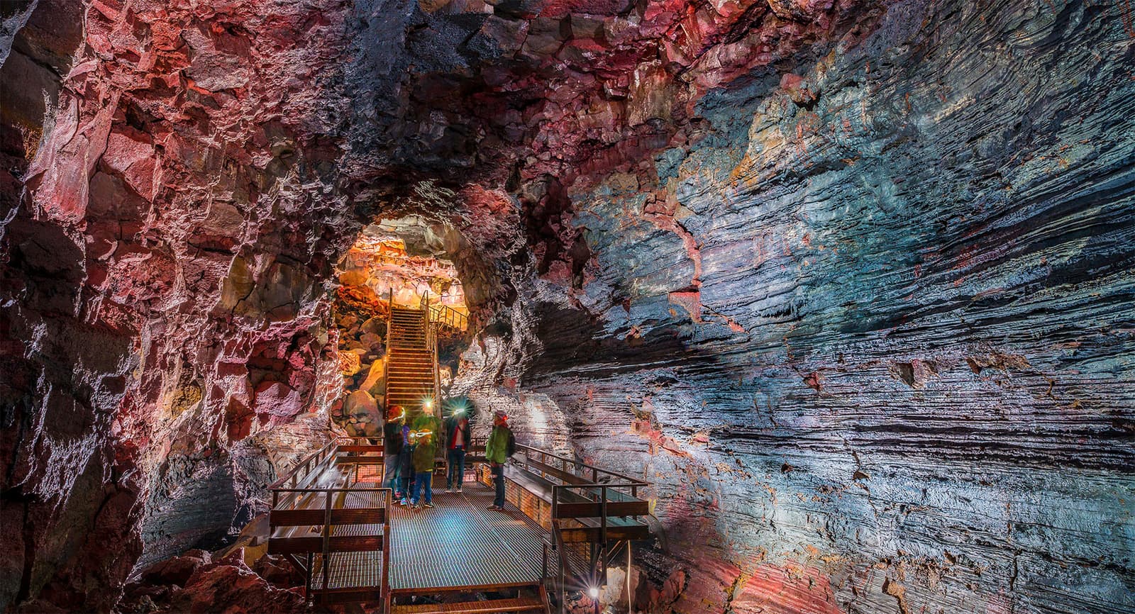 Visitors on a lit platform inside the colorful basalt passage of Raufarhólshellir lava tunnel.
