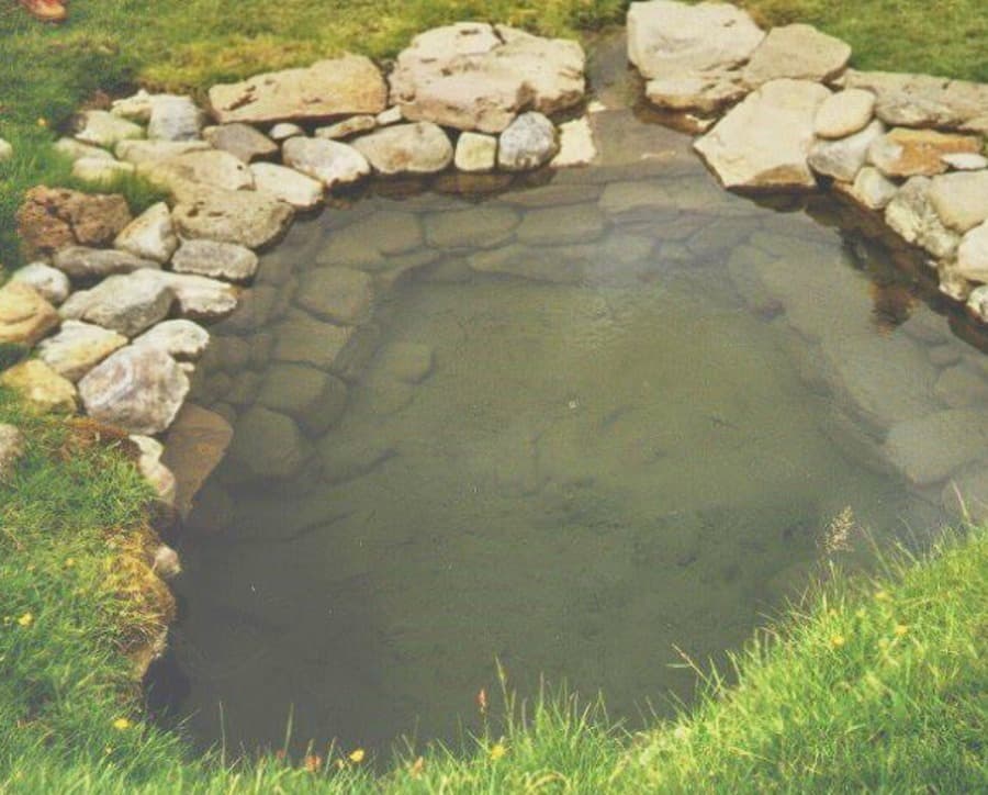Close view of Bishop's Pool at Reykir in Hjaltadalur, edged with stones and grass.