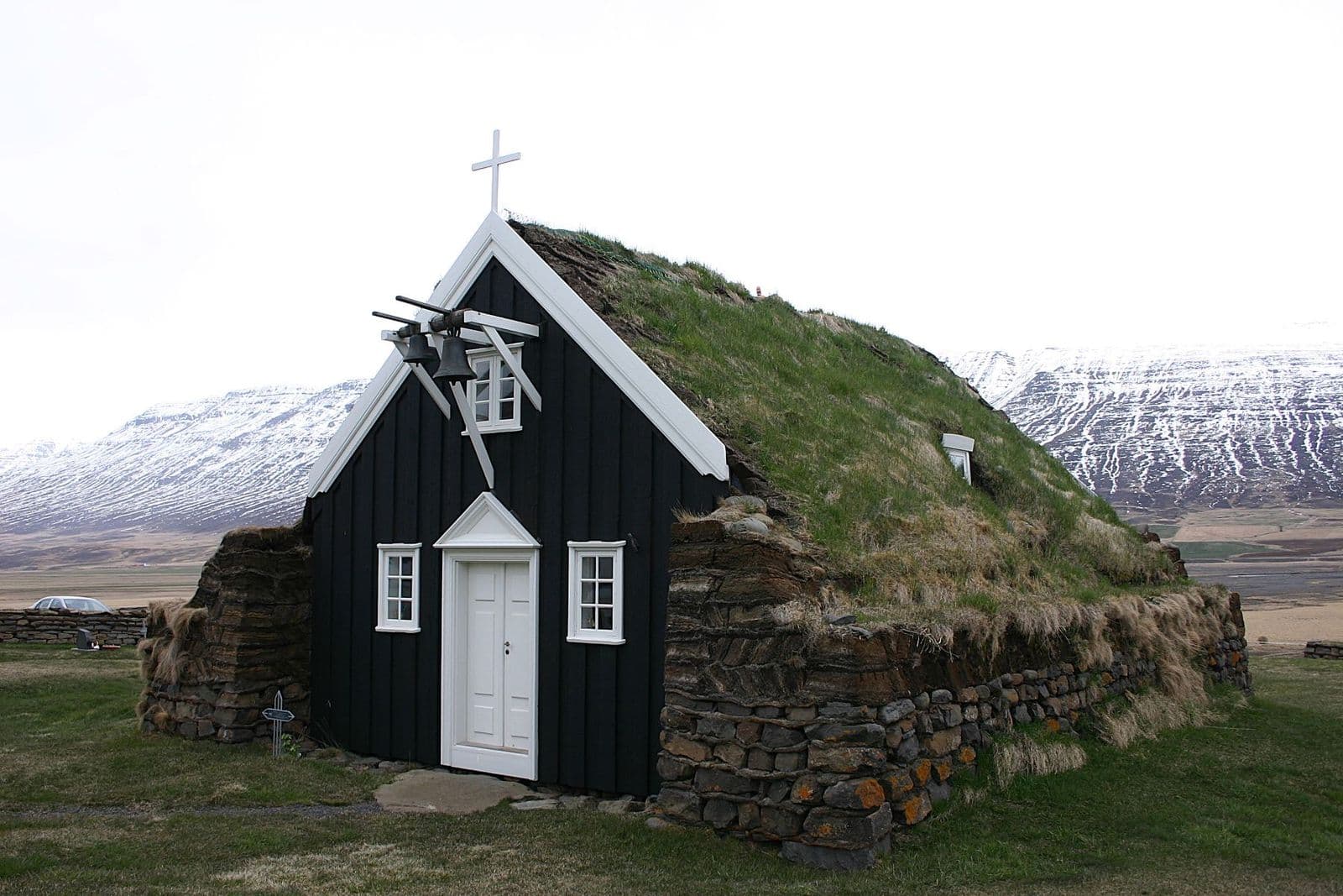 Saurbæjarkirkja turf church with black timber gable, turf roof, stone walls, and Eyjafjörður mountains behind it.