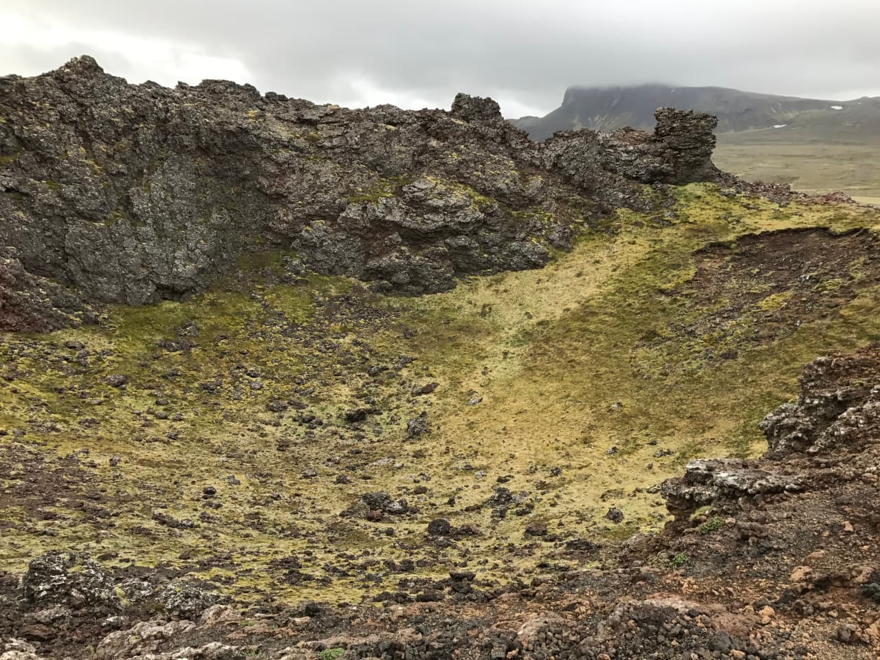 Rough lava and mossy ground inside the Saxhóll crater area under low cloud.