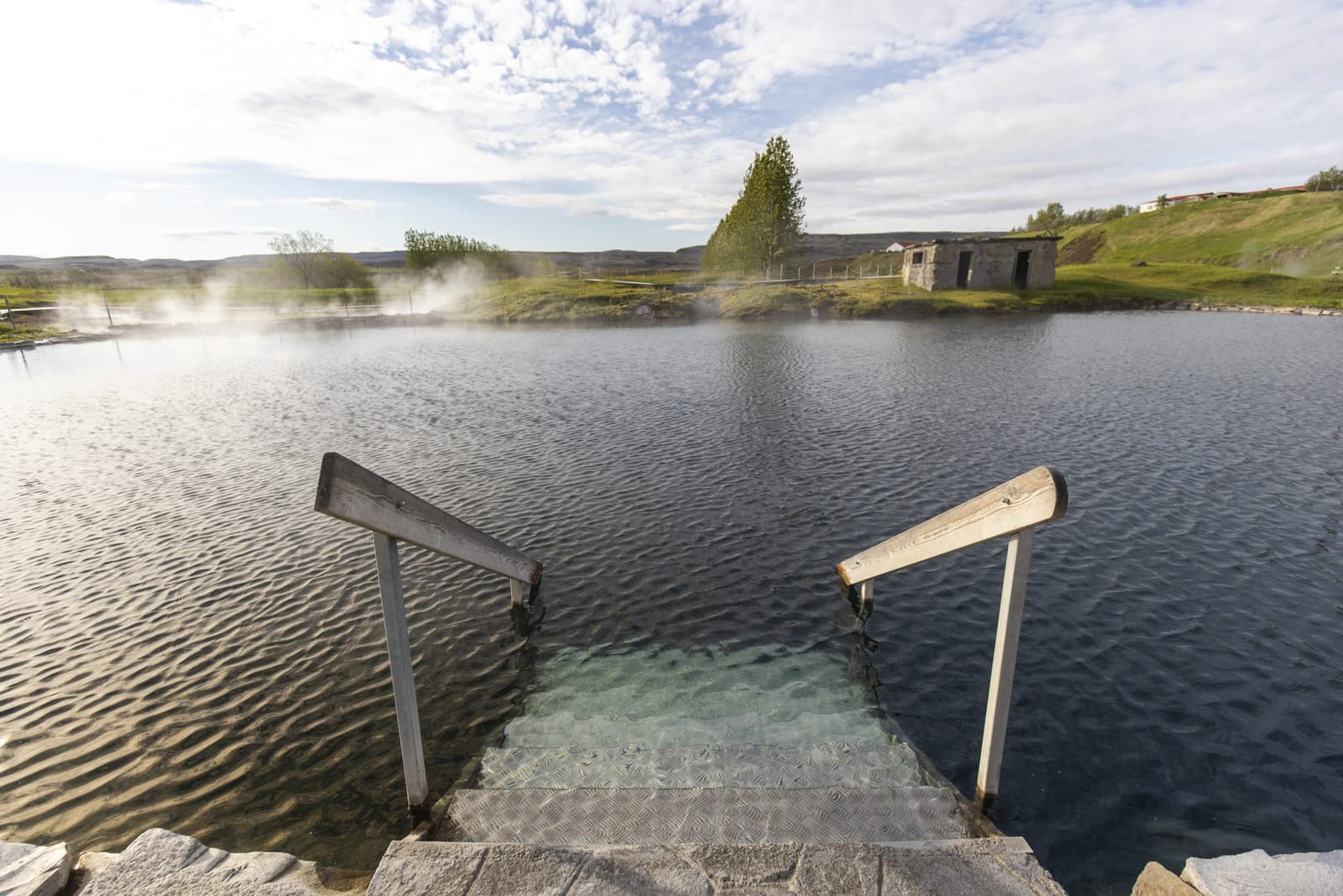 Empty pool steps at Secret Lagoon with steam rising from the surrounding geothermal area.