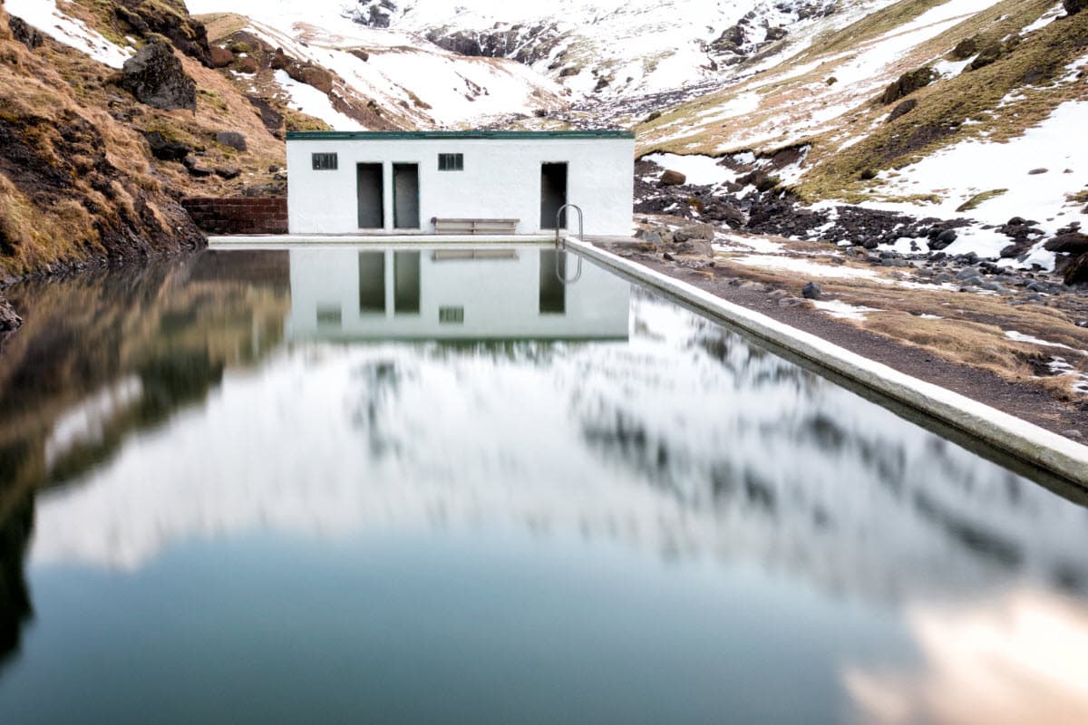 Seljavallalaug pool and white changing building below snowy mountain slopes.