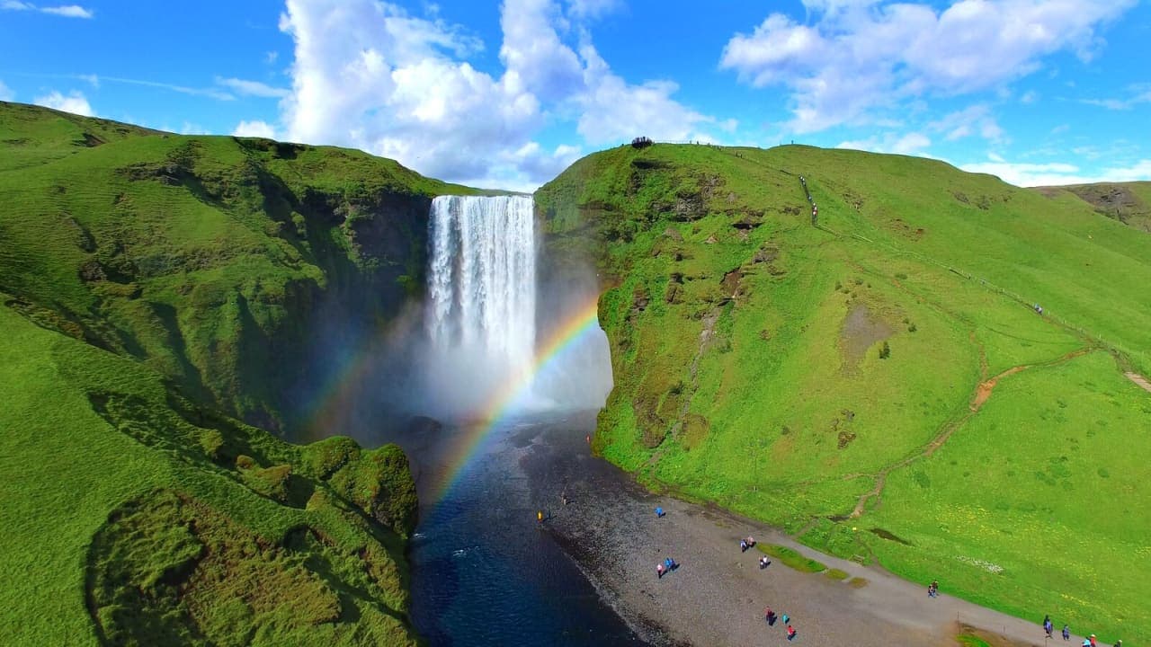 Rainbow mist in front of Skogafoss waterfall below green South Iceland cliffs.