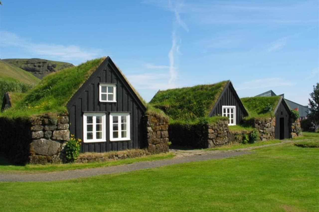 Turf-roofed houses at Skógar Museum below green South Iceland hills.
