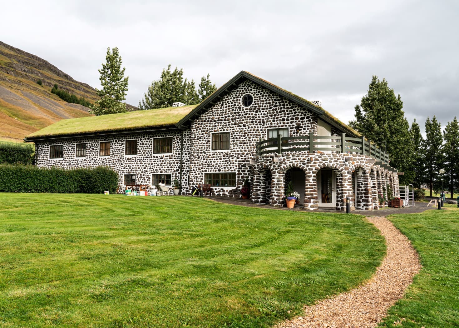 Gunnarshús at Skriðuklaustur with a turf roof, stone-patterned walls, lawn, footpath, and Fljótsdalur slopes behind it.