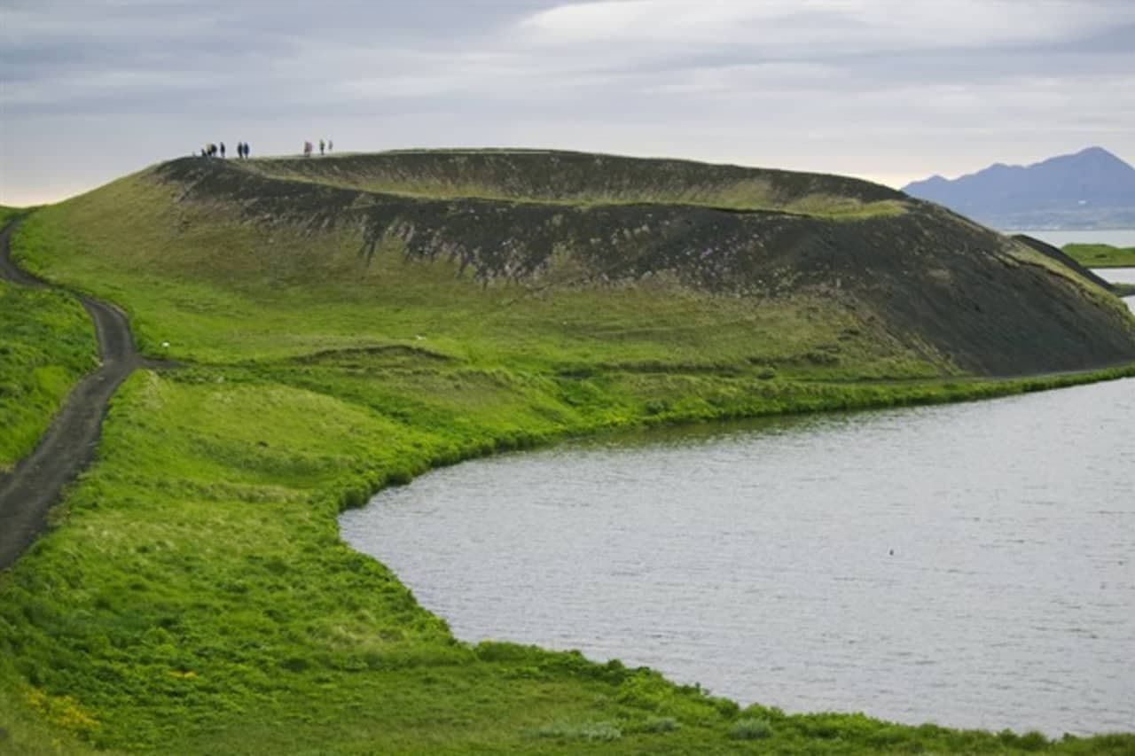 Large grassy Skútustaðagígar pseudocrater beside Lake Mývatn with people on the rim path.
