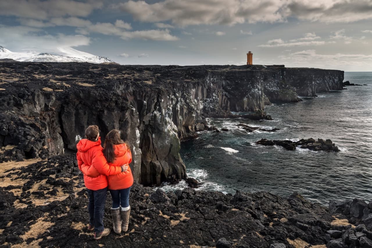 People looking over Snæfellsnes sea cliffs with Snæfellsjökull visible in the distance.