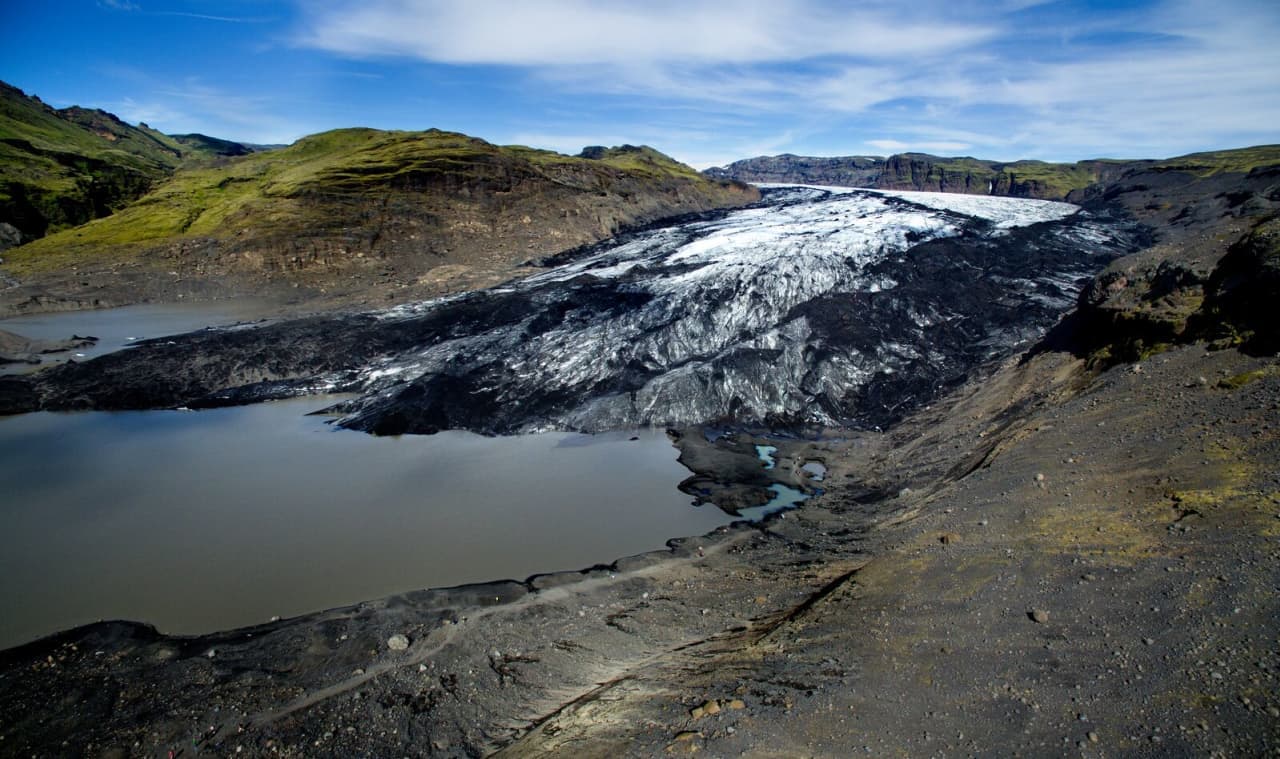 Sólheimajökull Glacier descending into a gray lagoon below dark South Iceland hills