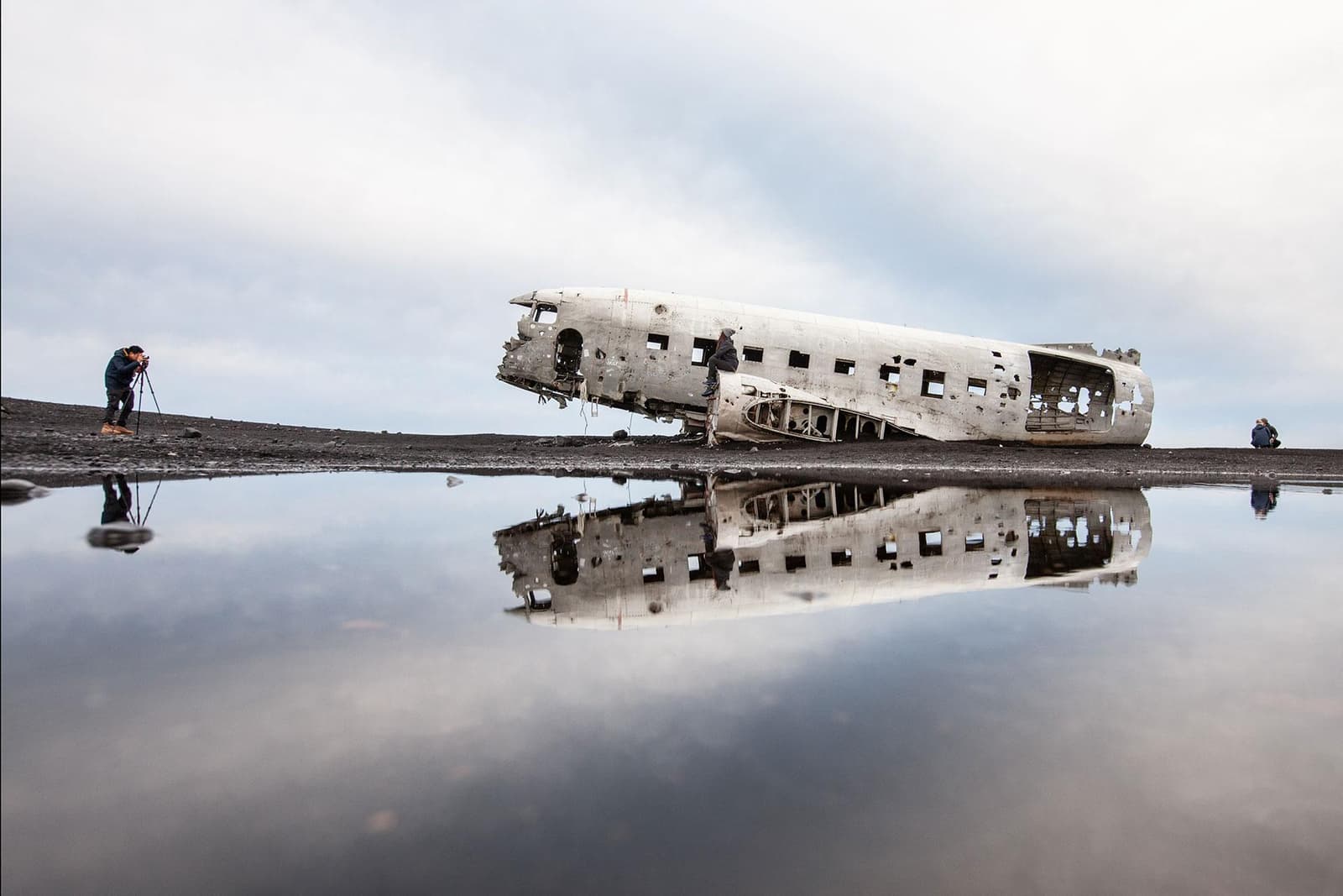 The DC-3 wreck reflected in shallow water on the Sólheimasandur black sand plain.
