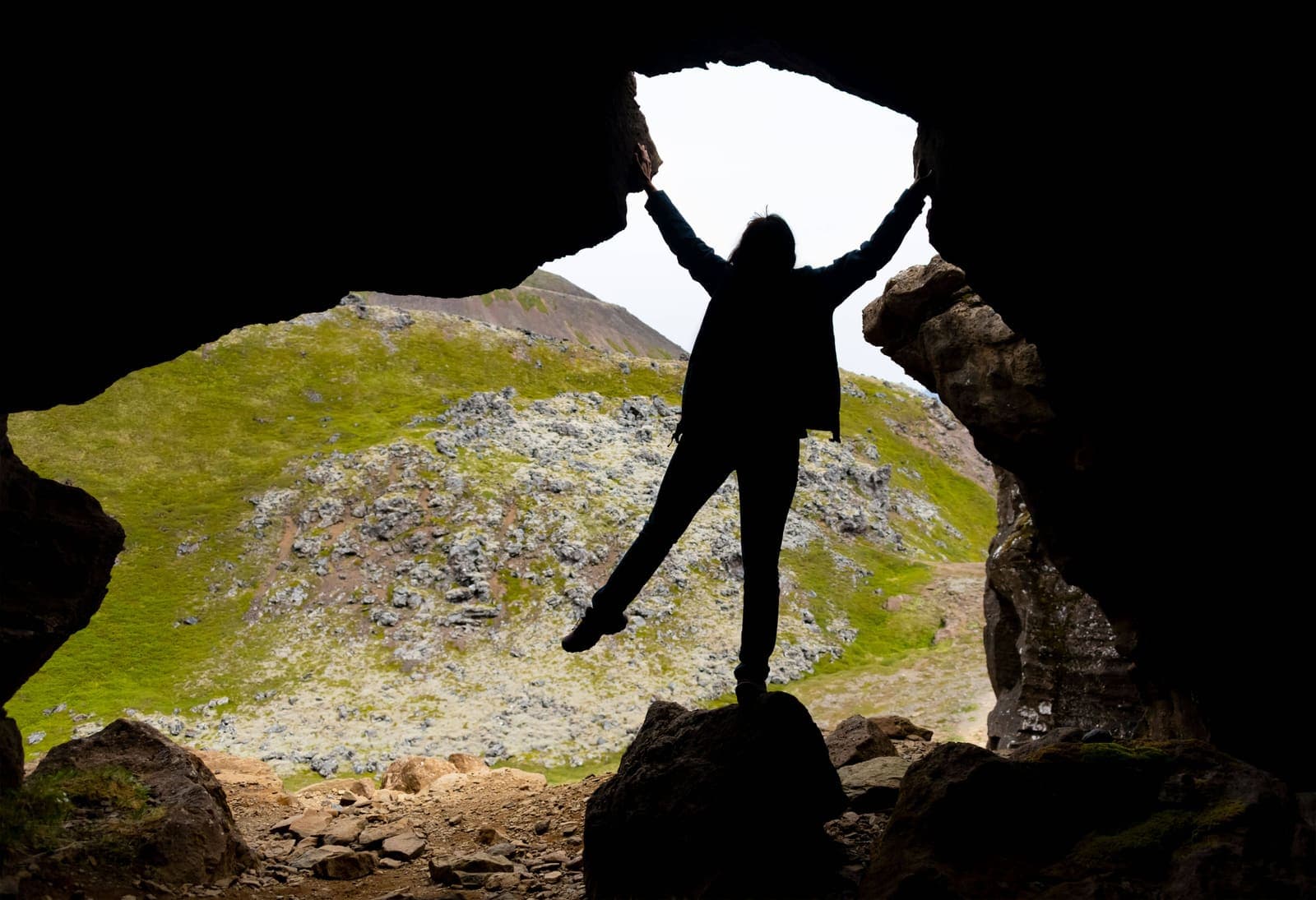 Silhouetted visitor standing inside Sönghellir Cave with the rocky Snæfellsnes slope visible outside.