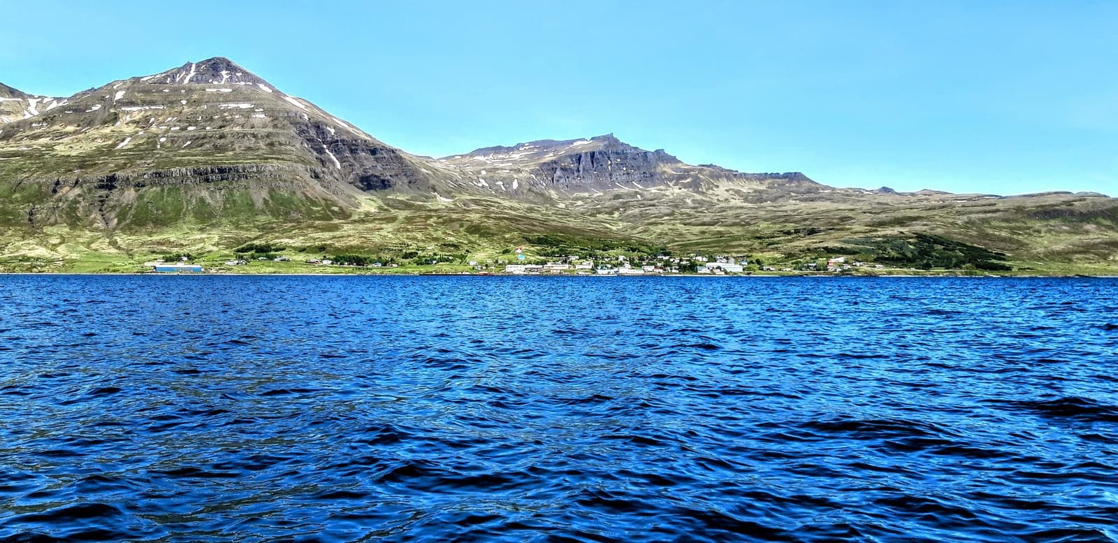 View across the fjord toward Stöðvarfjörður with the village lined below steep Eastfjords mountains.
