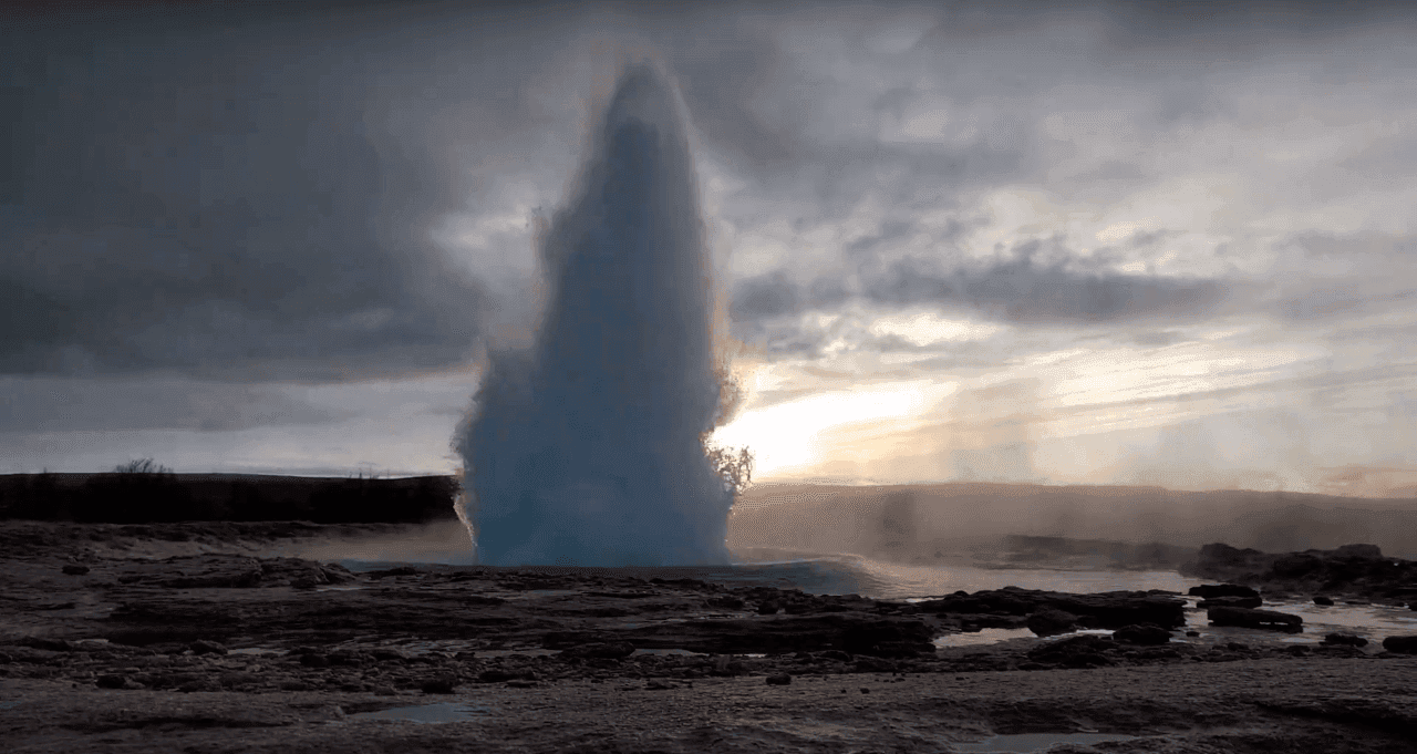 A tall Strokkur eruption rising from the Geysir geothermal area under cloudy light.