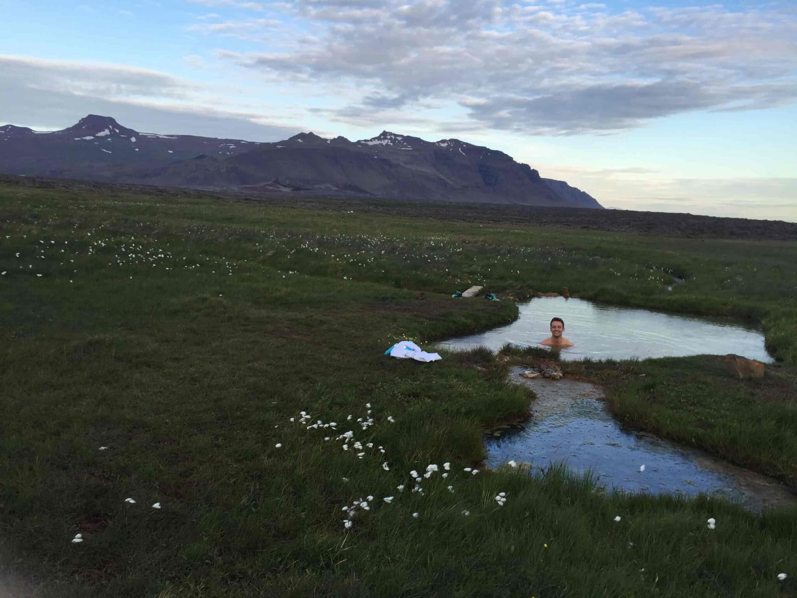 Small geothermal pool at Sturlungalaug Hot Springs with mountains beyond the Snæfellsnes-side grassland.