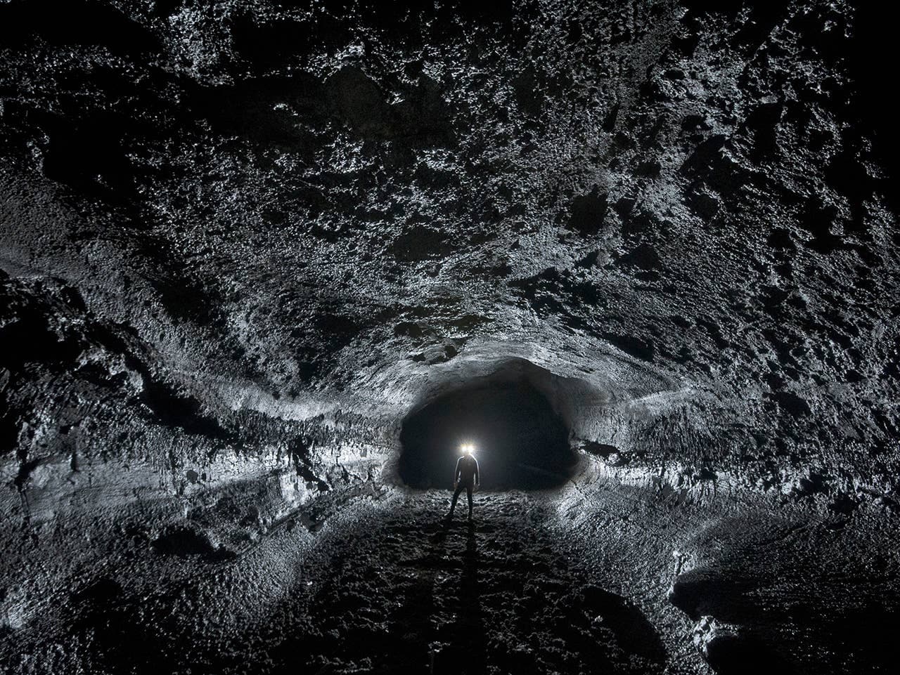 Person with a headlamp standing inside the dark Surtshellir lava cave in West Iceland.