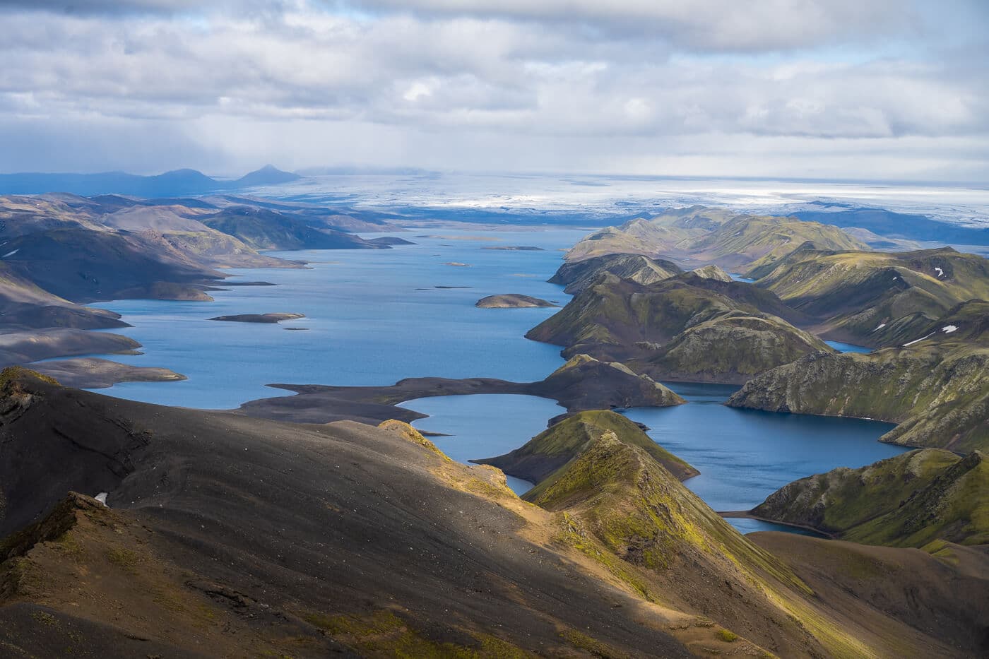 View over Langisjór from Sveinstindur with blue lake arms, dark ridges, and Vatnajökull beyond.