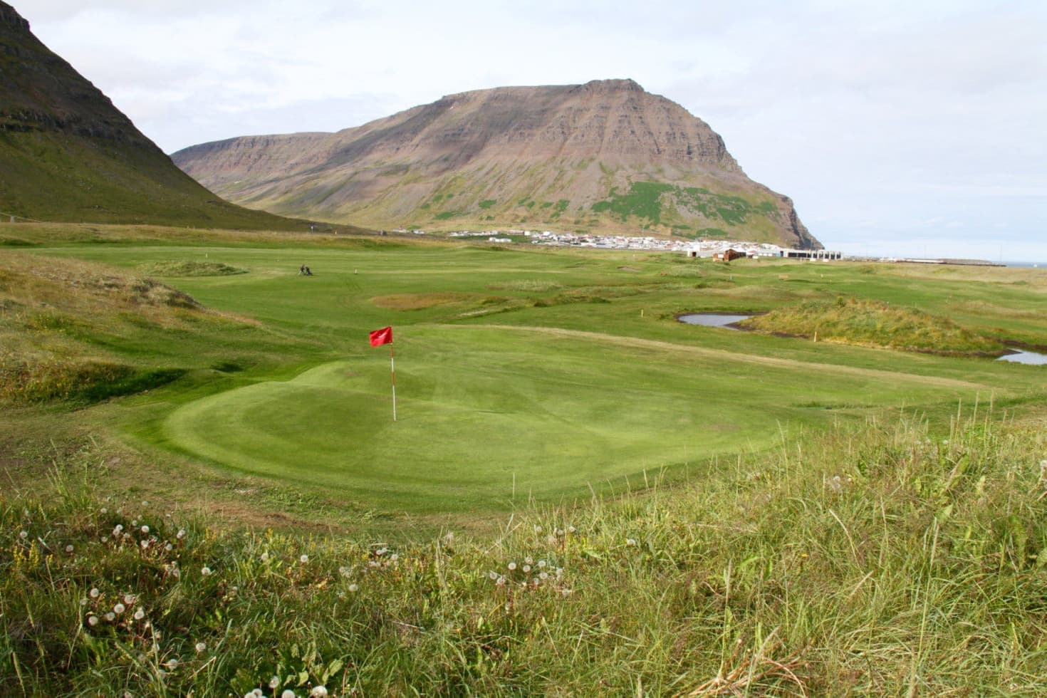 Green Syðridalur valley and Bolungarvík landscape below steep Westfjords mountains.