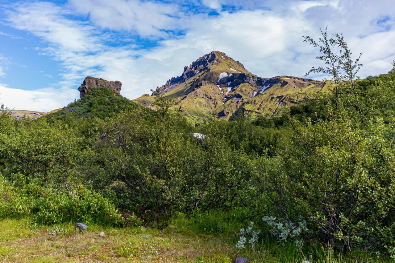 Green Þórsmörk birch scrub below steep volcanic mountains and patches of snow.
