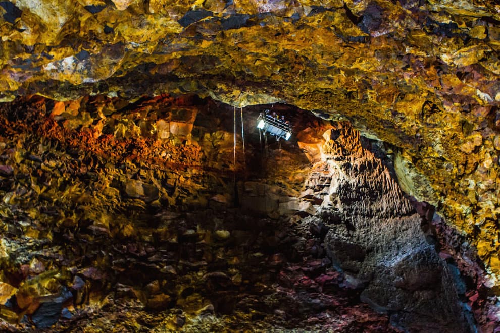 Wide view of the orange and black Þríhnúkagígur magma chamber with a narrow blue-lit opening above.