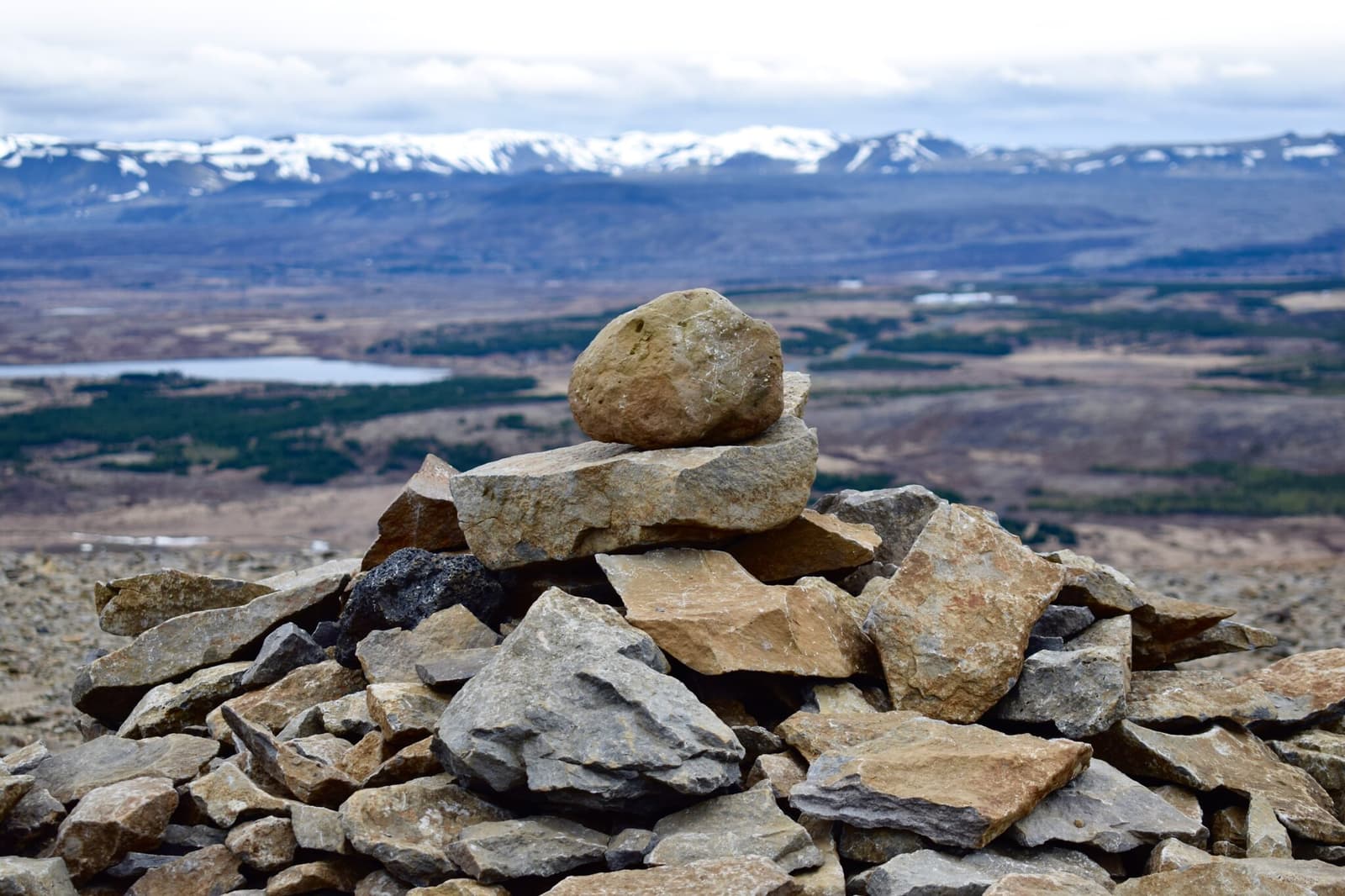 Rock cairn on Úlfarsfell with Mosfellsbær hills blurred behind it.