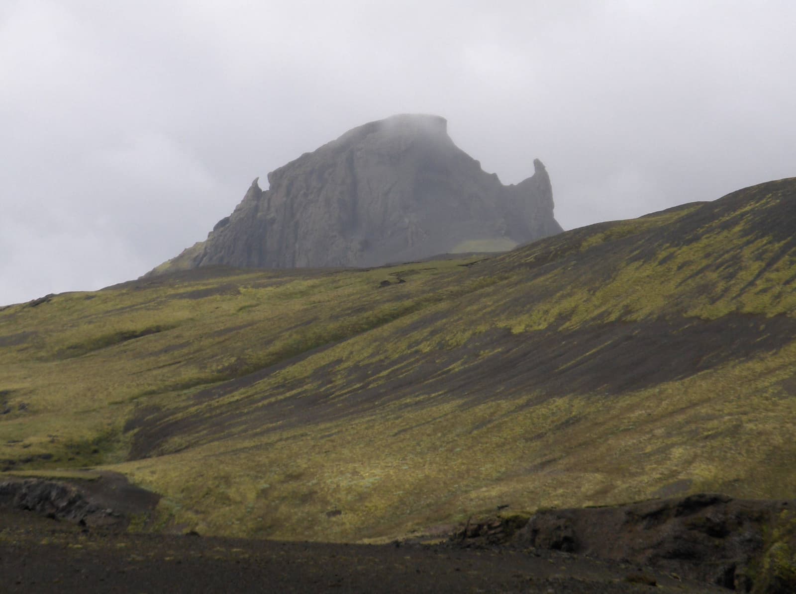 Einhyrningur rising through low cloud above green and black highland slopes in South Iceland.