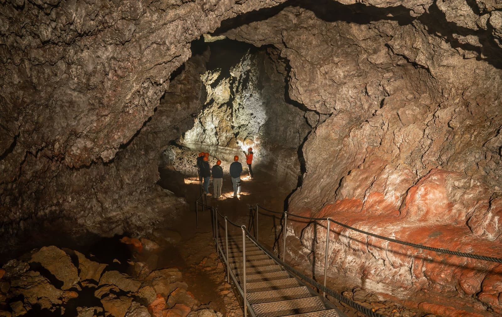 Guided visitors inside Vatnshellir Cave below rough lava walls and a metal walkway.