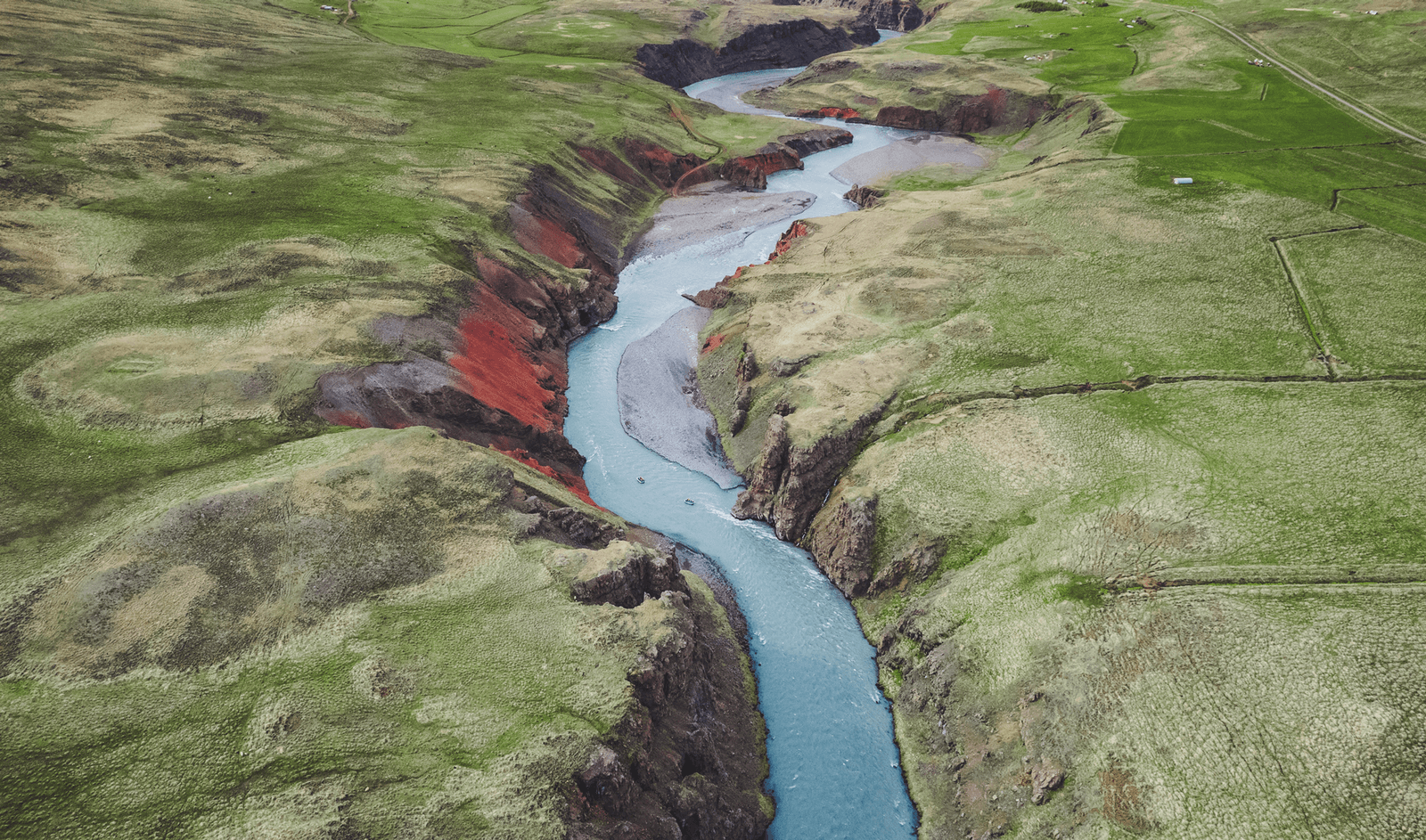 Aerial view of Vestari Jökulsá cutting through a green Skagafjörður canyon with rafts on the pale glacial river.