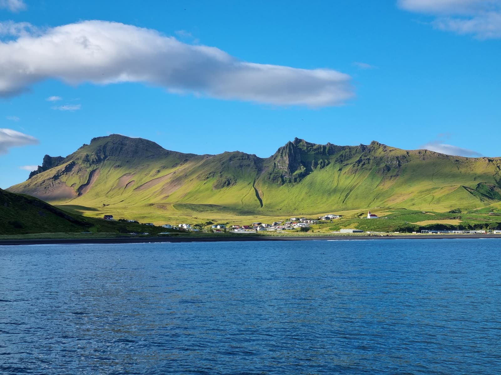 Vík coastline and village with steep green slopes under a long cloud.