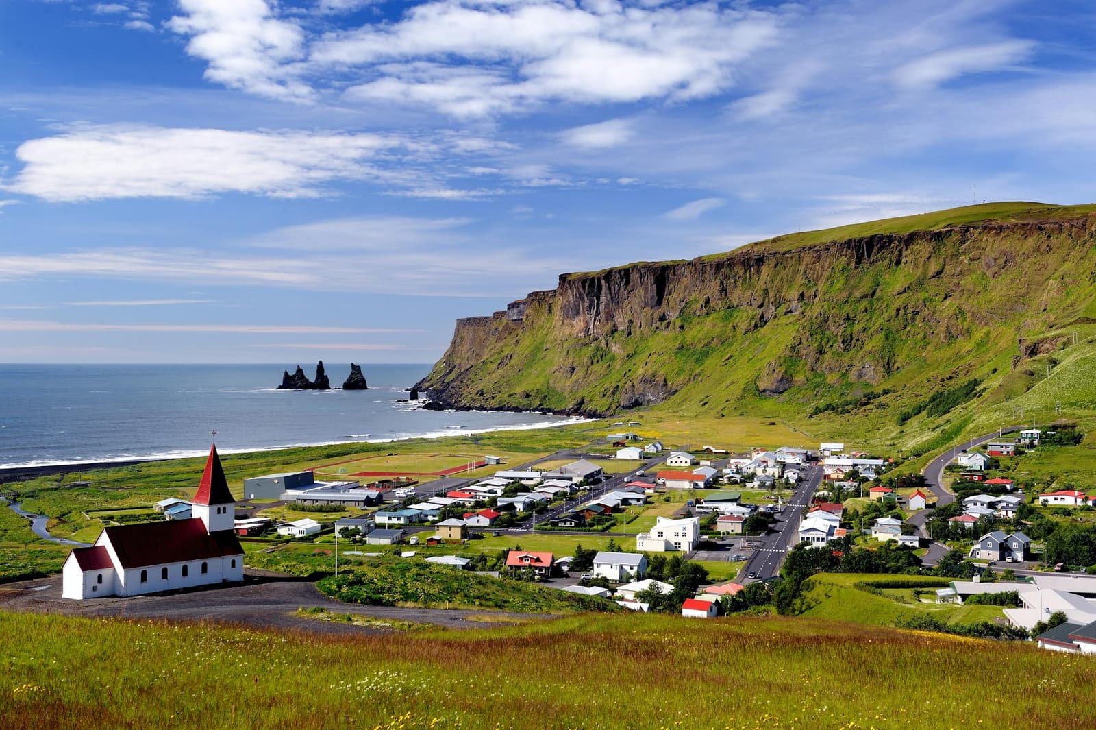 Vík village, church, Reynisdrangar, and the black-sand coast seen together from above town.