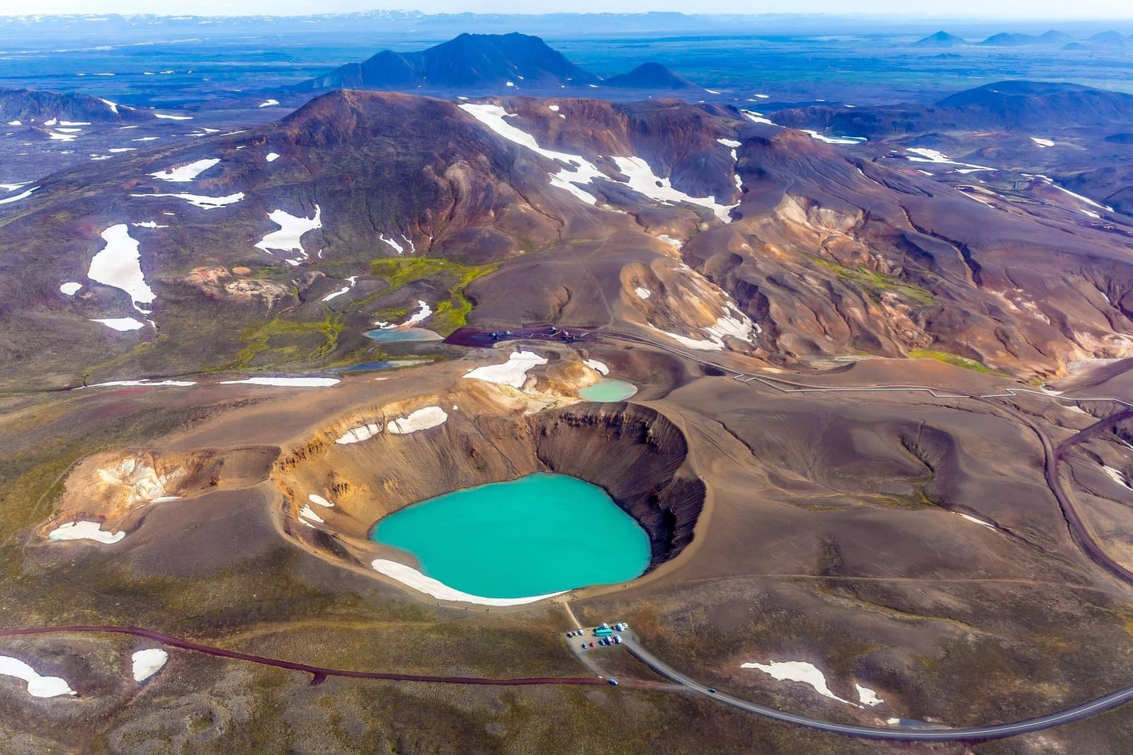 Aerial view of Víti crater, snow patches, roads, and Krafla volcanic terrain in North Iceland.