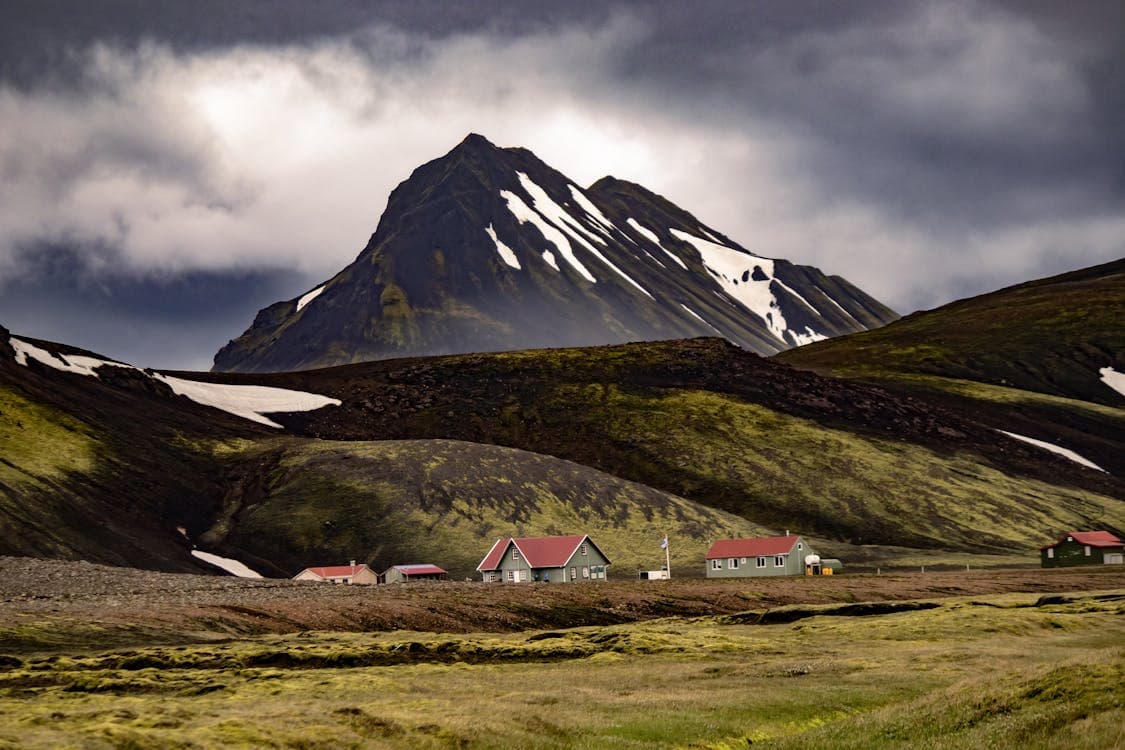 Dramatic Iceland mountain landscape with red-roofed huts under cloudy skies