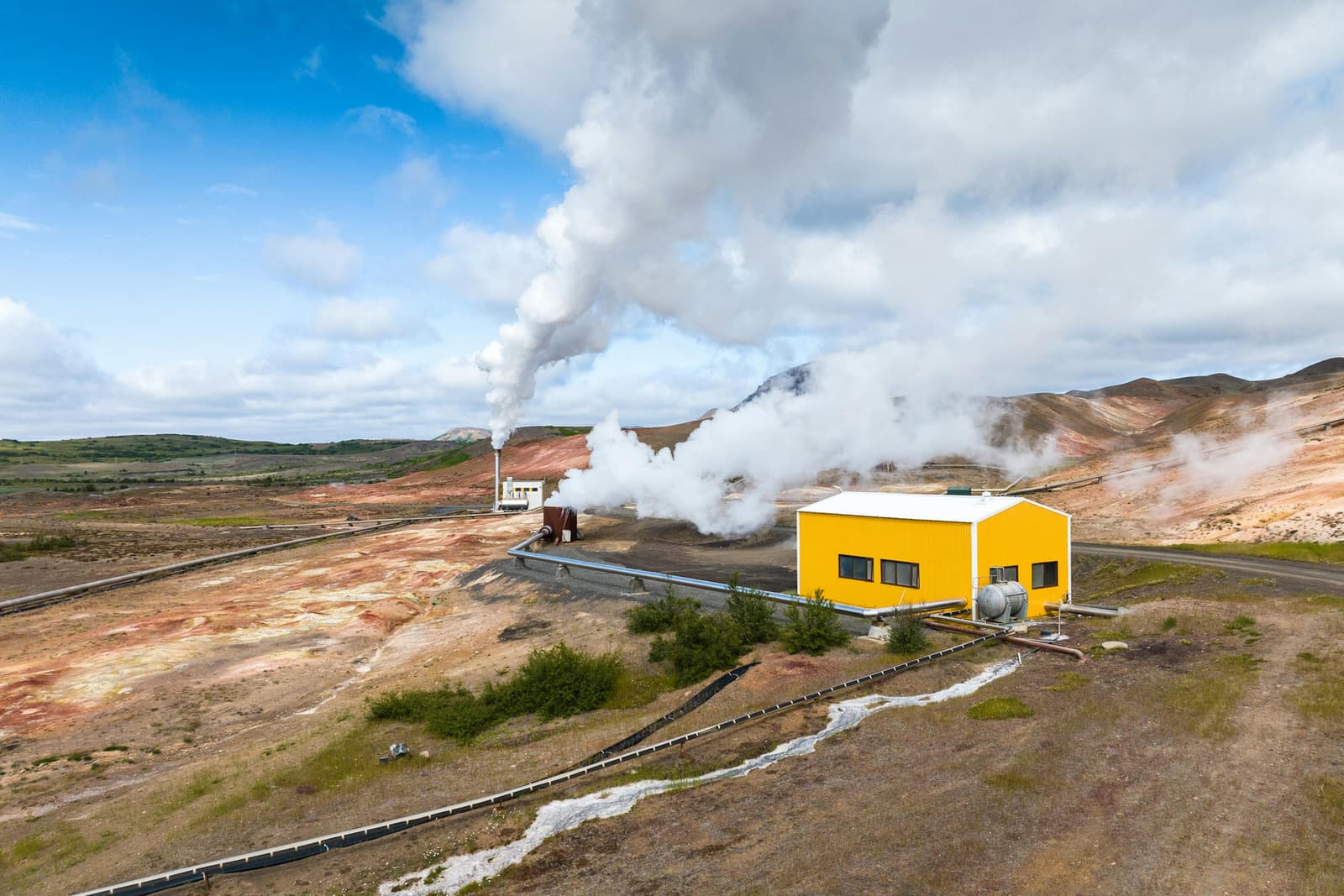 Steam plumes rising from Bjarnarflag Geothermal Station pipes and yellow buildings below Námafjall.